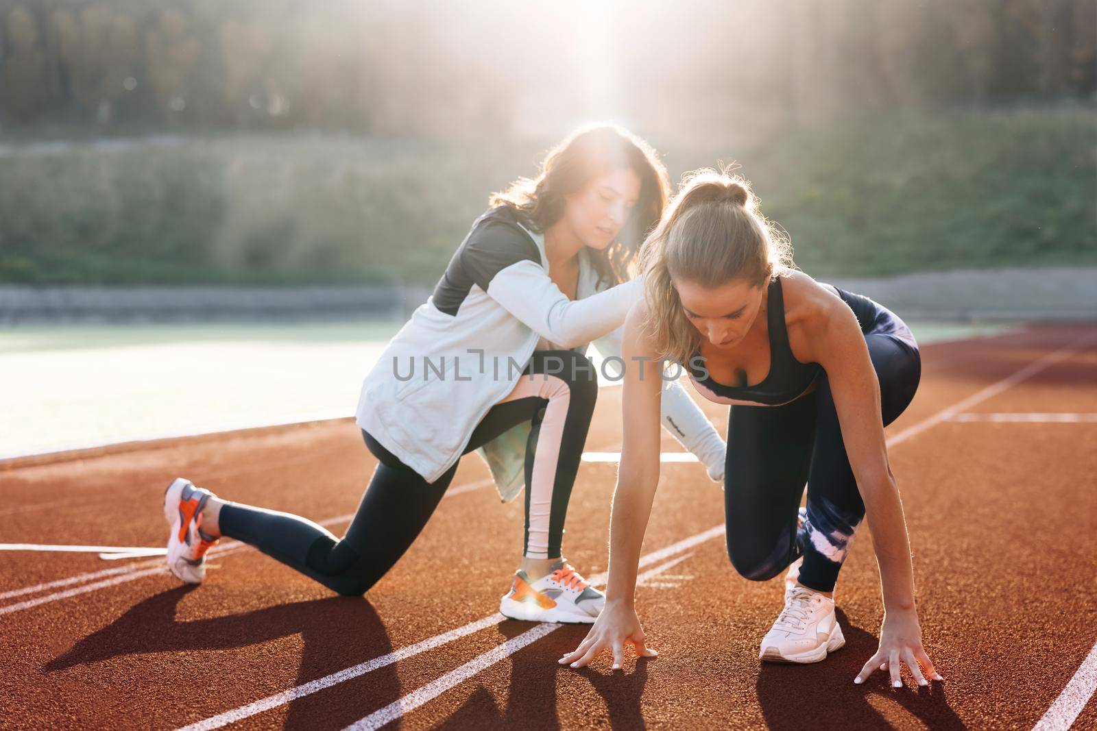 Caucasian Athlete ready to start. Young female runner with personal trainer preparing for blasting off in mist on sports track of stadium, training before competition. Sportswoman. Cardio exercises.