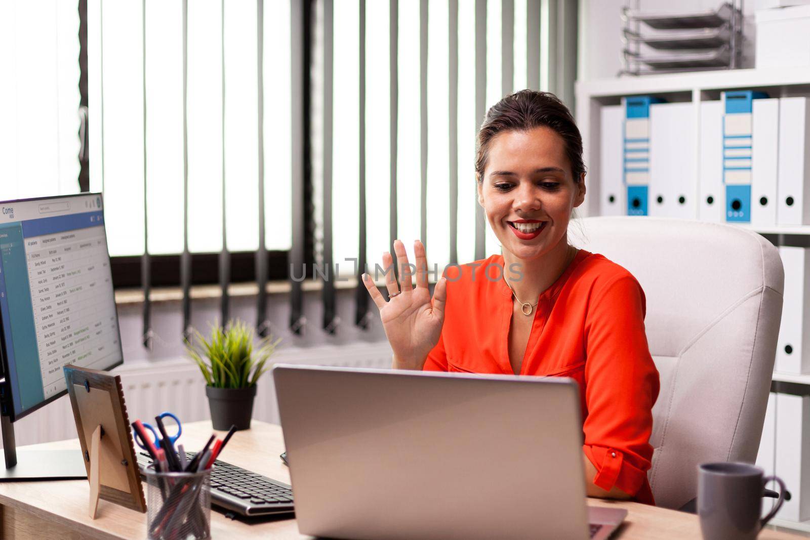 Businesswoman waving at notebook webcam during video conference with coworkers. Entrepreneur using internet connection for video meeting with coworkers looking at webcam.