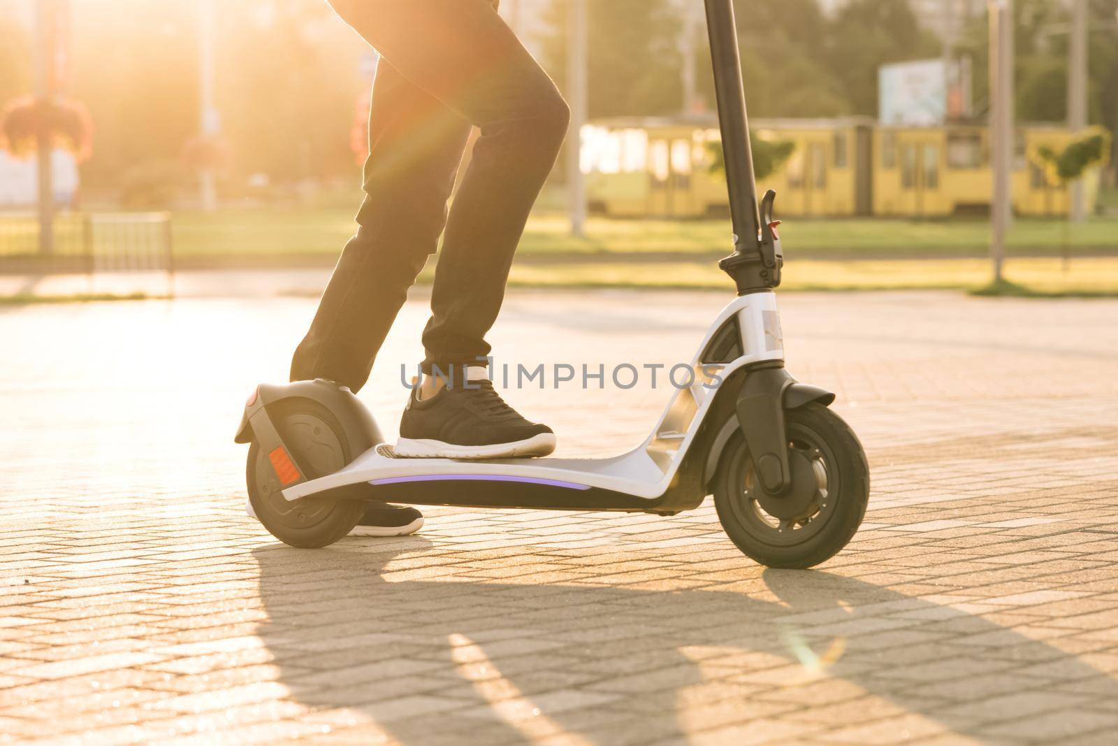 Legs hipster in black sneakers riding an electric scooter road to work the modern way. Fast speed driving electric transport. E-scooter rider, man ride sharing or rent personal eco transportation.