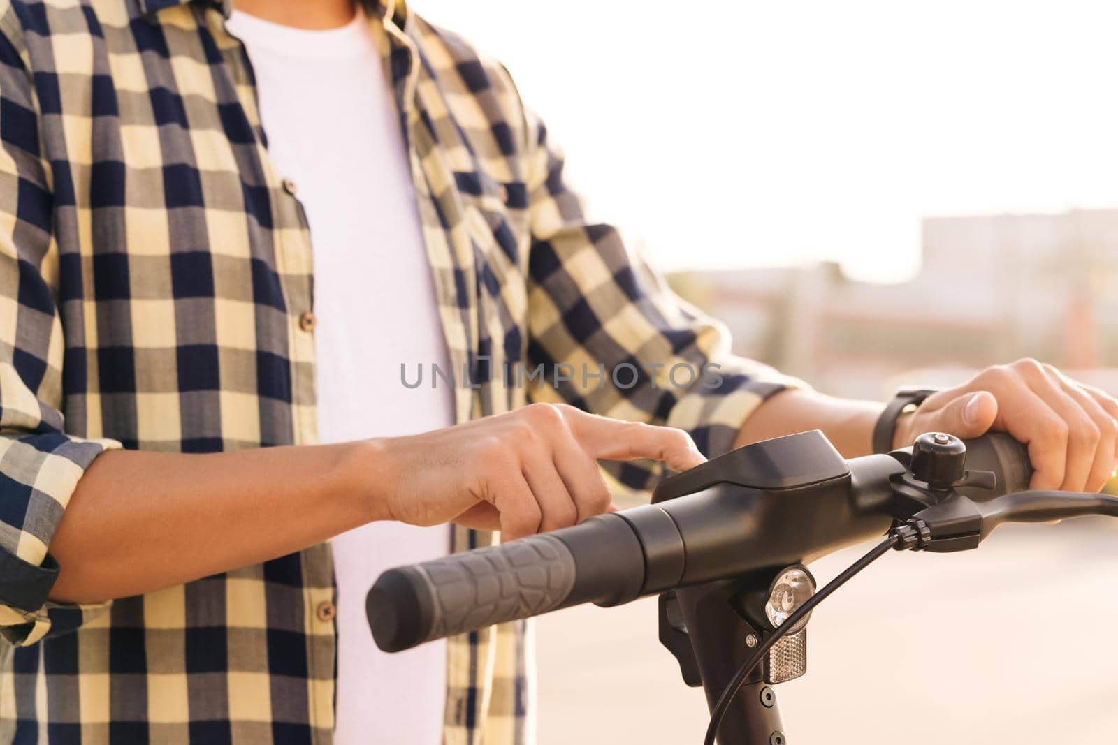 Young man is pushing start button of modern gadget and driving along street of city. Closeup male hands on wheel of electric scooter. Ecological alternative transport concept.