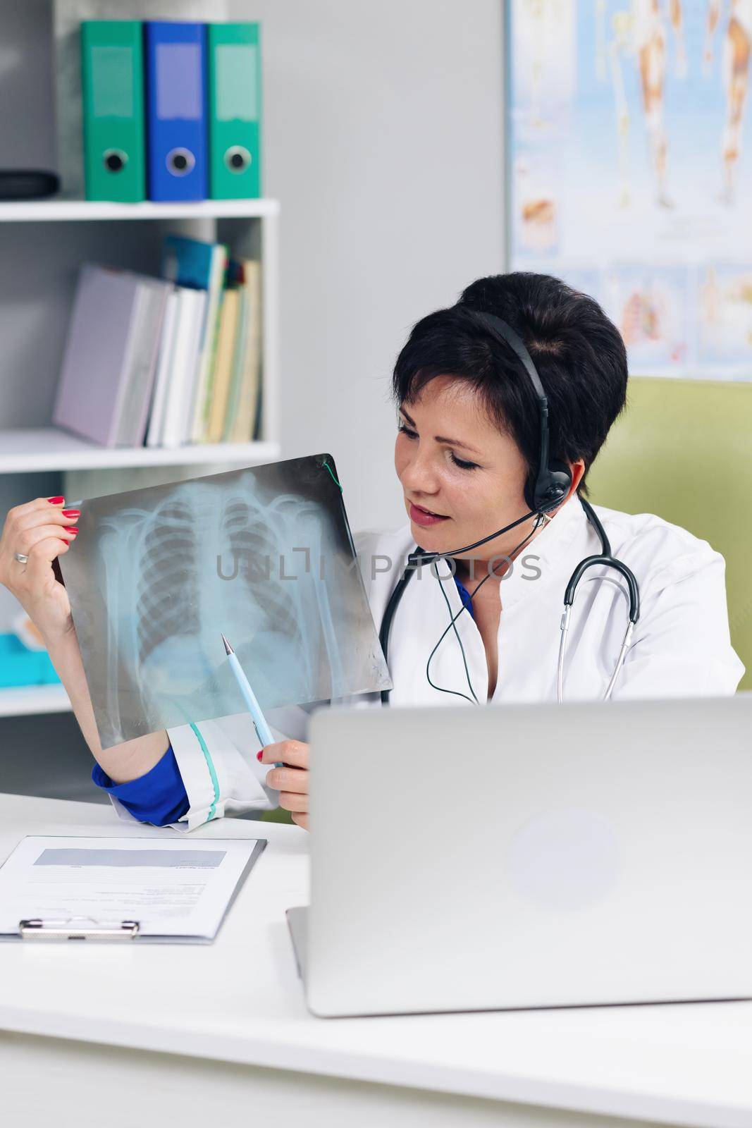 Female medical doctor wears white coat, headset video calling distant patient on laptop. Doctor talking to client using virtual chat computer app. Telemedicine, remote healthcare services concept.