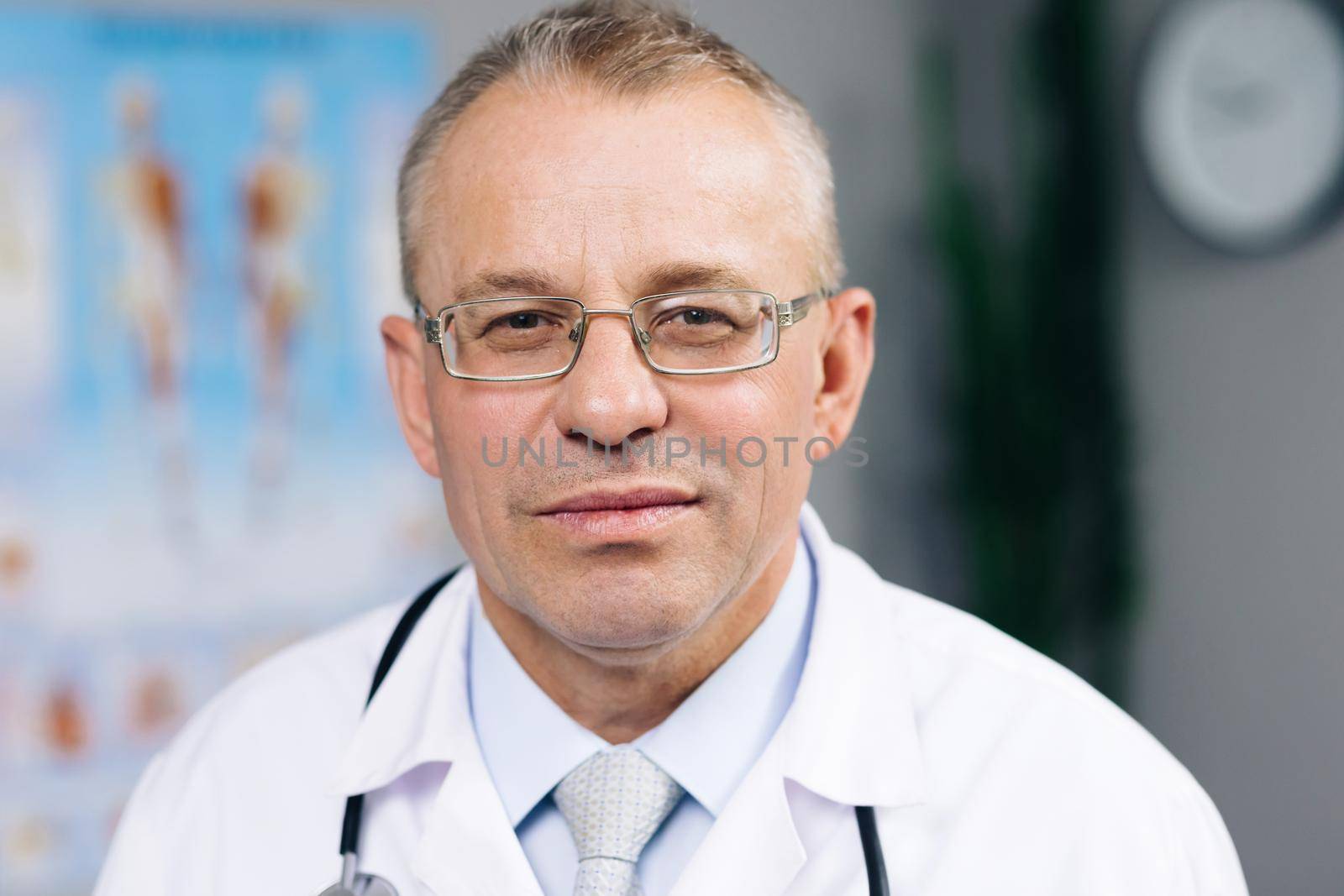 Portrait of Caucasian Family Medical Doctor in Glasses is in Health Clinic. Successful Physician in White Lab Coat Looks at the Camera and Smiles in Hospital Office by uflypro