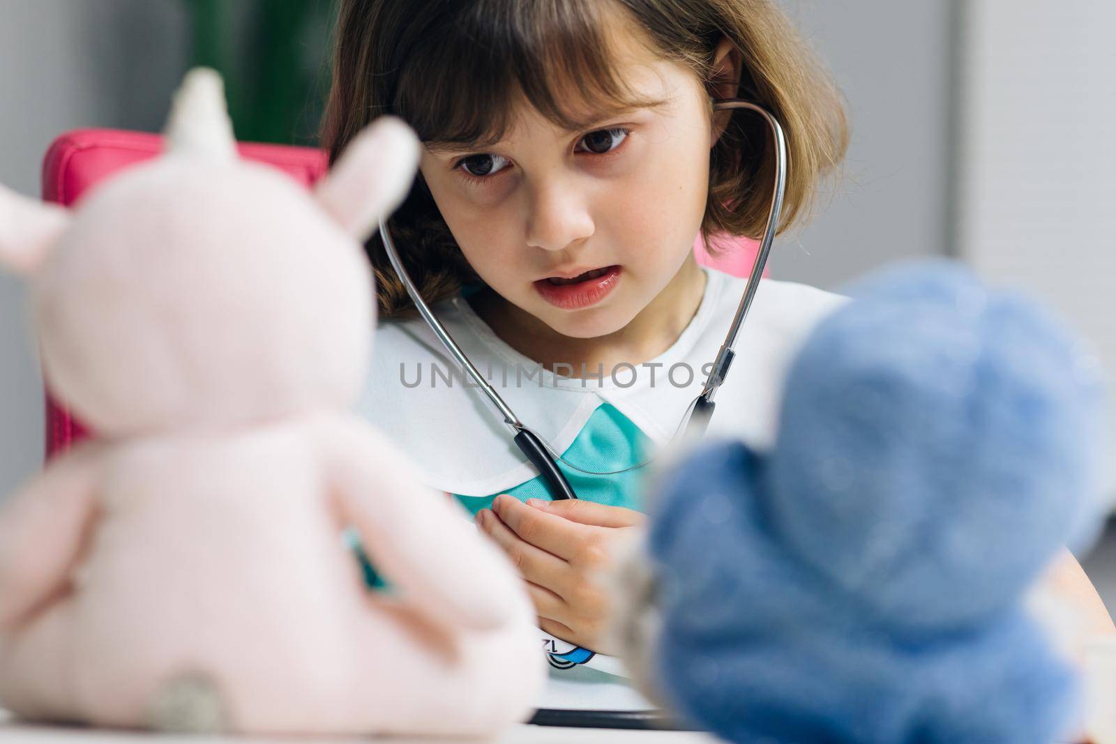 Cute adorable little preschool kid girl wear medical uniform holding stethoscope listening sick toy patient. Smart small child playing hospital game as doctor pretend nurse concept. by uflypro