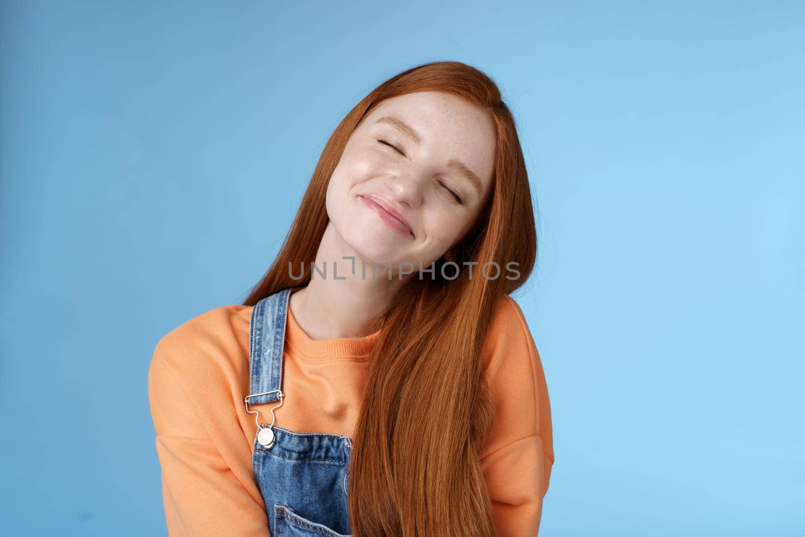 Dreamy kind silly redhead smiling happy girl straight long ginger hair daydreaming imagine romantic moment close eyes smiling delighted tilting head look joyful, standing blue background by Benzoix