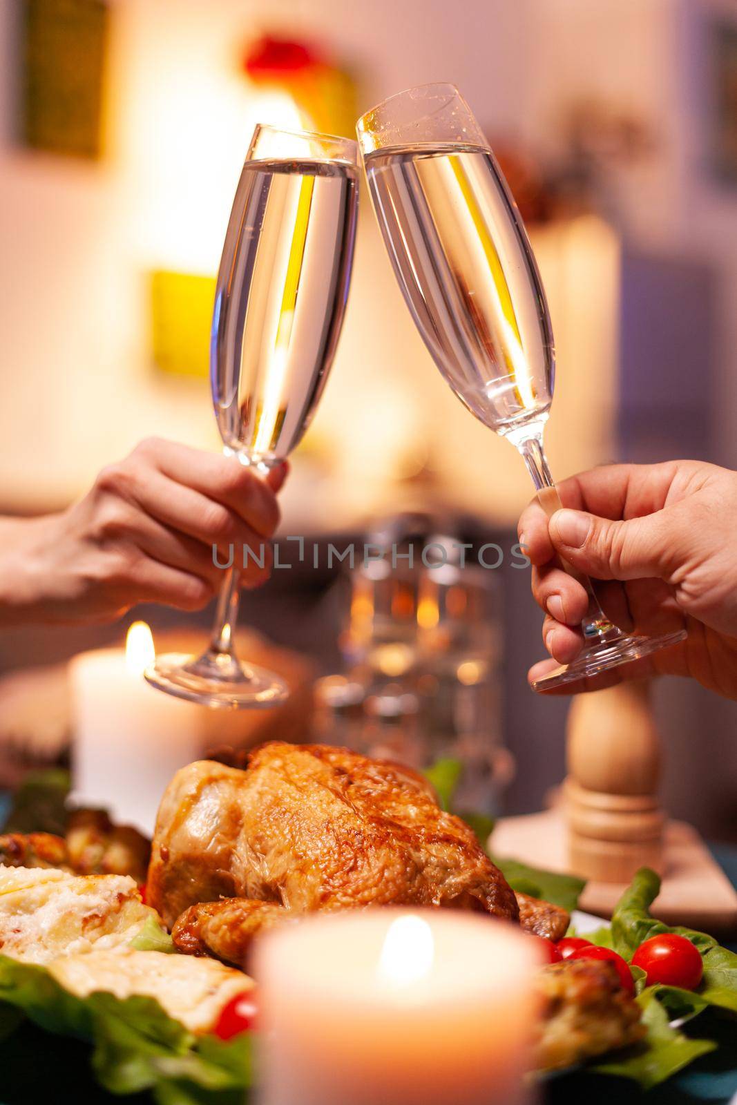 Closeup of couple hands clinking glass of wine during christmas dinner sitting at dining table in xmas decorated kitchen. Happy romantic family celebrating christmas holiday together