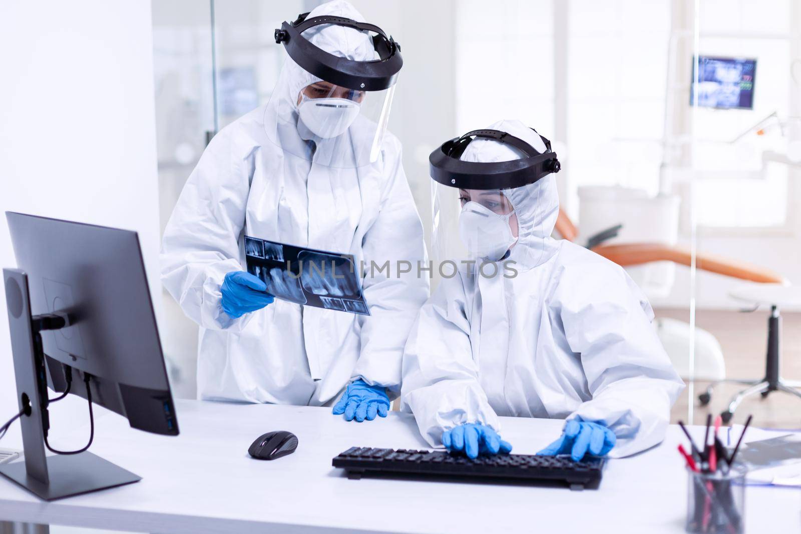 Dentist doctor and nurse in ppe suit against covid-19 and nurse holding teeth x-ray. Medical specialist wearing protective gear against coronavirus during global outbreak looking at radiography in dental office.