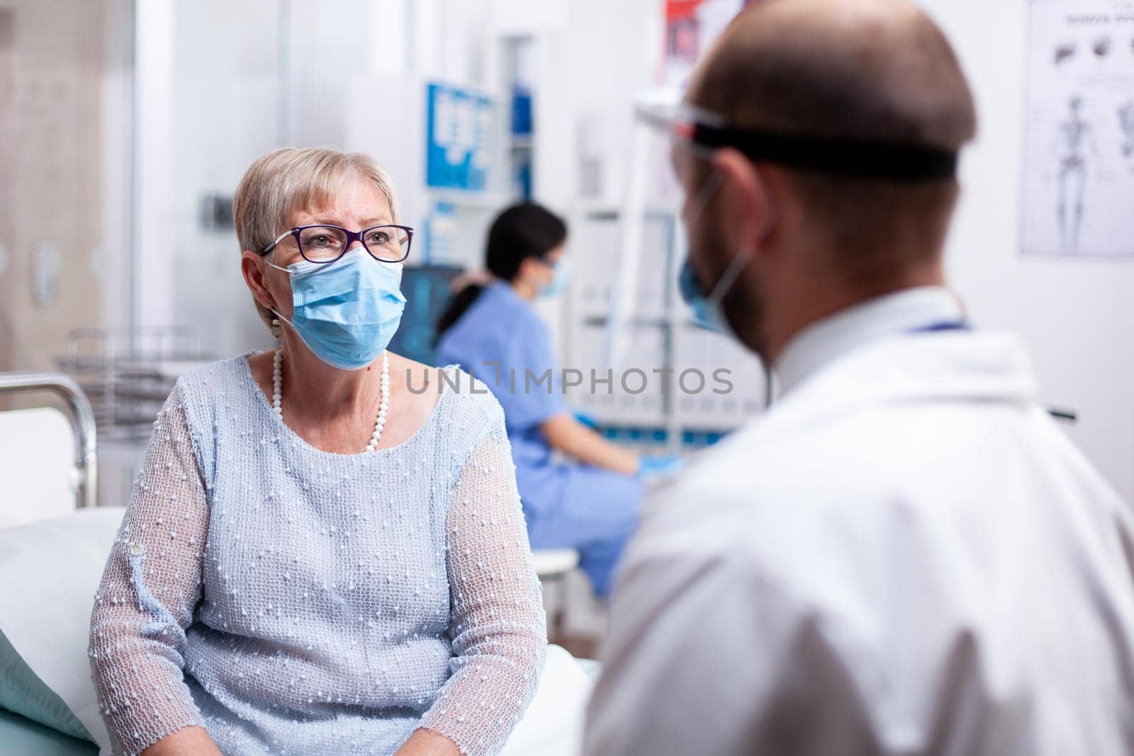 Sick old woman wearing protective mask during consultation for coronavirus outbreak in hospital cabinet. Global health crisis, medical system during pandemic, sick elderly patient in private clinic.