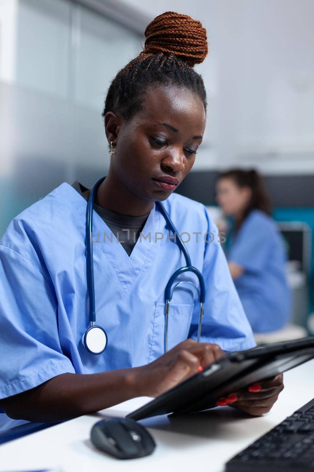 African american nurse in medical uniform analyzing sickness prescription on tablet computer working in hospital office. Physician asisstance monitoring disease writing healthcare treatment