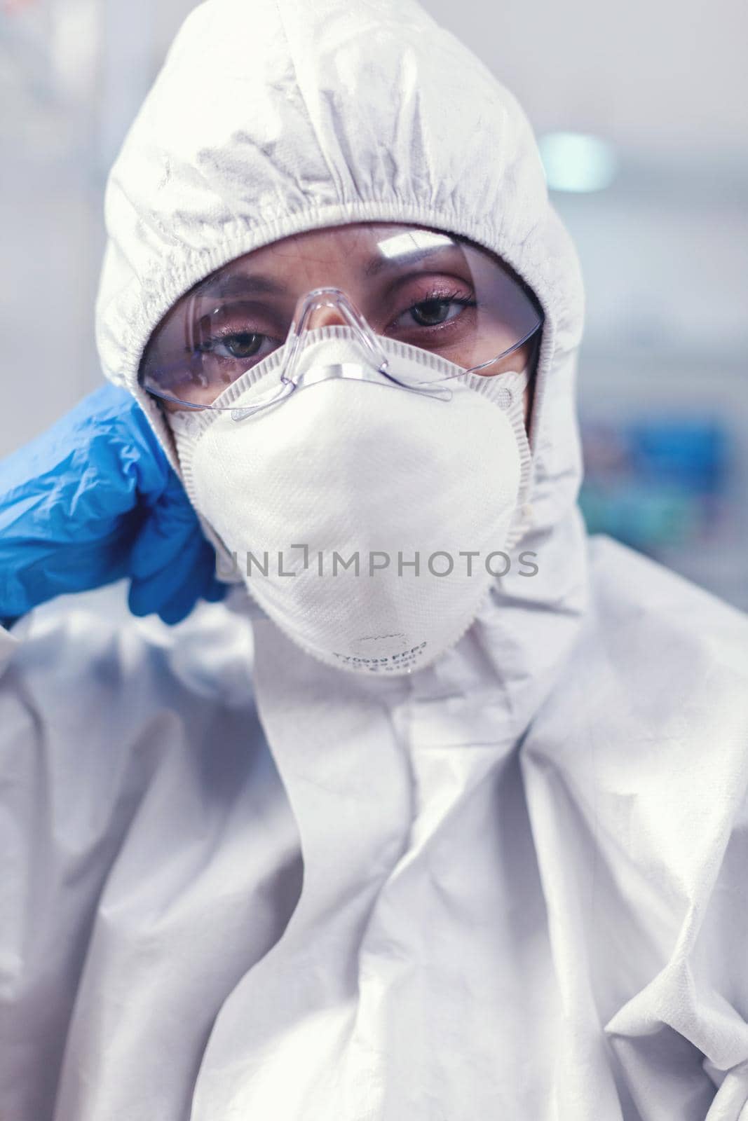 Tired laboratory doctor with overall suit looking at camera in equipped lab. Overworked woman scientist in biotechnology laboratory wearing protective suit during global epidemic.