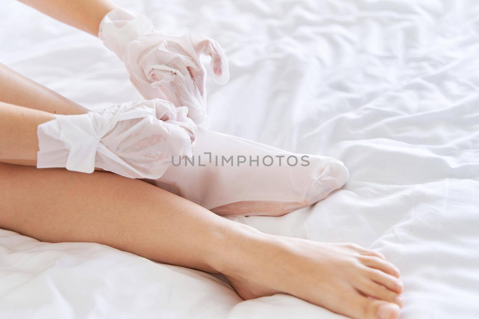 After a shower, a girl wrapped in a towel uses cosmetic gloves to moisturize the skin of her hands and feet. Cosmetic trends for body care at home by Try_my_best