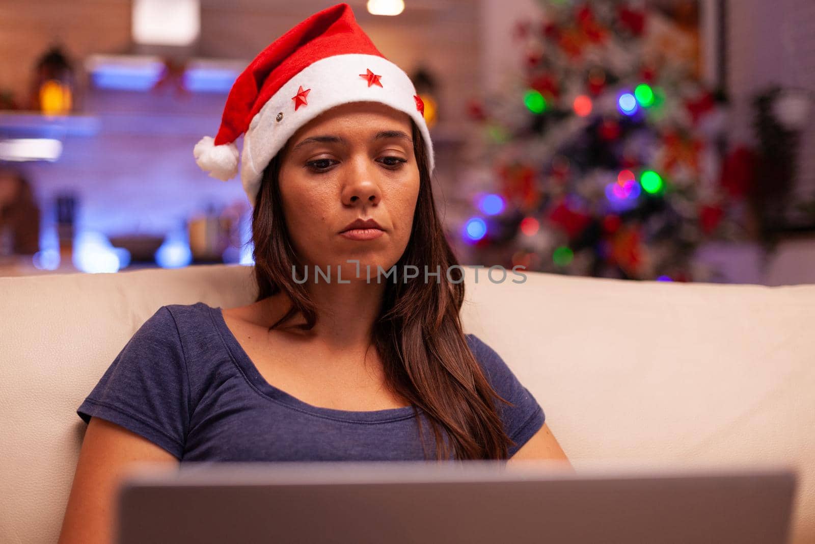 Woman looking at laptop screen reading business email during christmas holiday resting comfortable on couch in xmas decorated kitchen. Caucasian female browsing on social media. Winter season