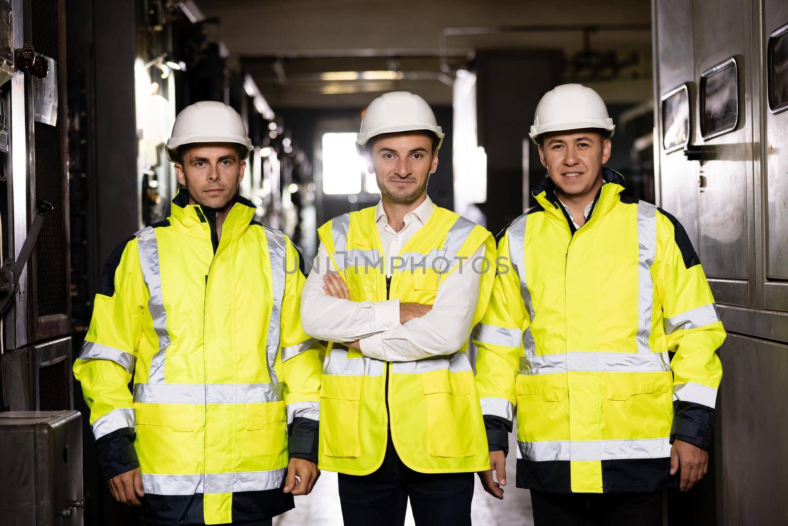 Workers wearing safety uniform and hard hat on unfocused background. Portrait of group of professional telecommunication industry engineers smiles and looks at the camera by uflypro