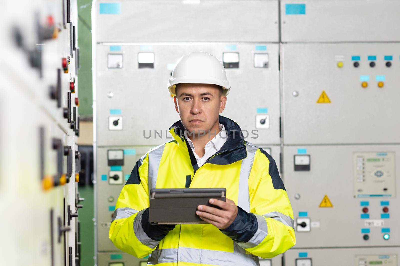 Asian man electrical engineer hold tablet monitoring electrical system in control room. Technician inspect to control panel screen system for generate electricity of factory in manufacture industrial.