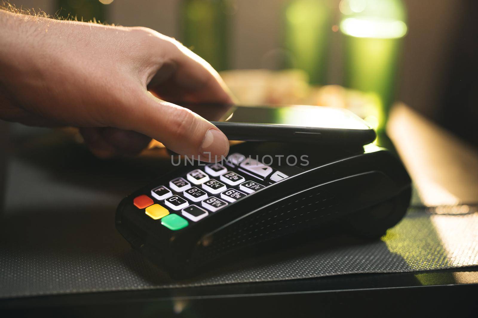 Young man using smartphone cashless wallet NFC technology to pay for order on wireless modern bank payment terminal in the bar. Contactless payment.