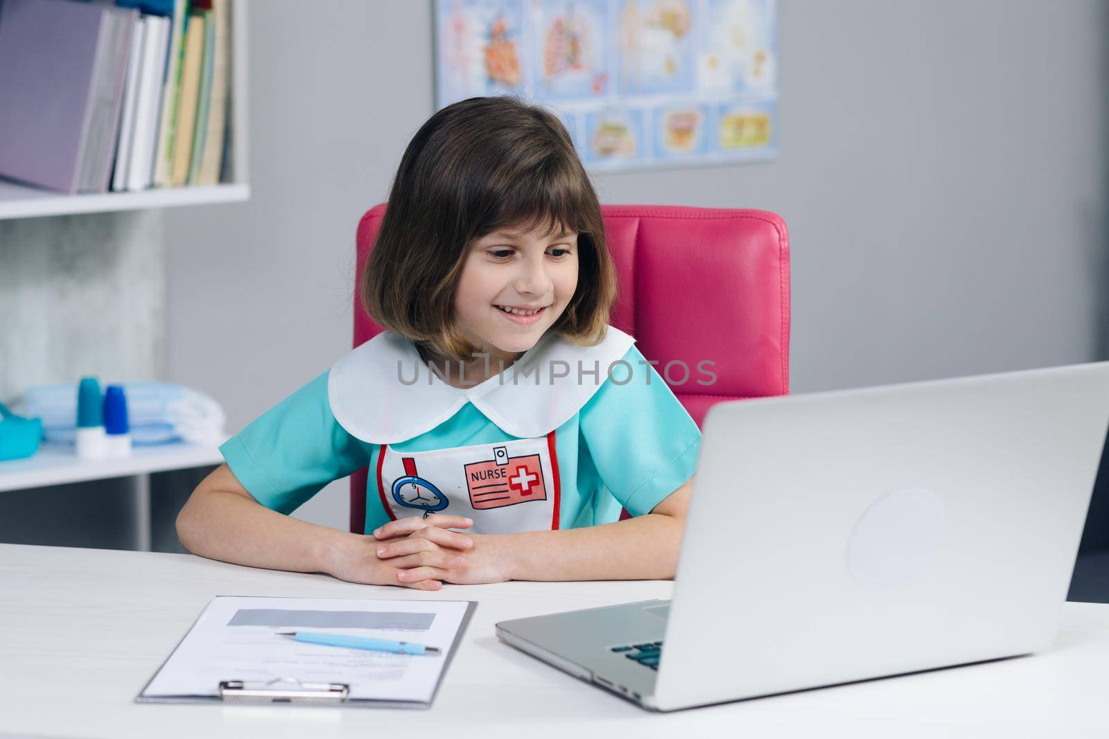 Happy cute small kid girl vlogger wear medical clothing talking to camera recording vlog for social media blog, video conference calling virtual friend having online meeting sitting on couch.
