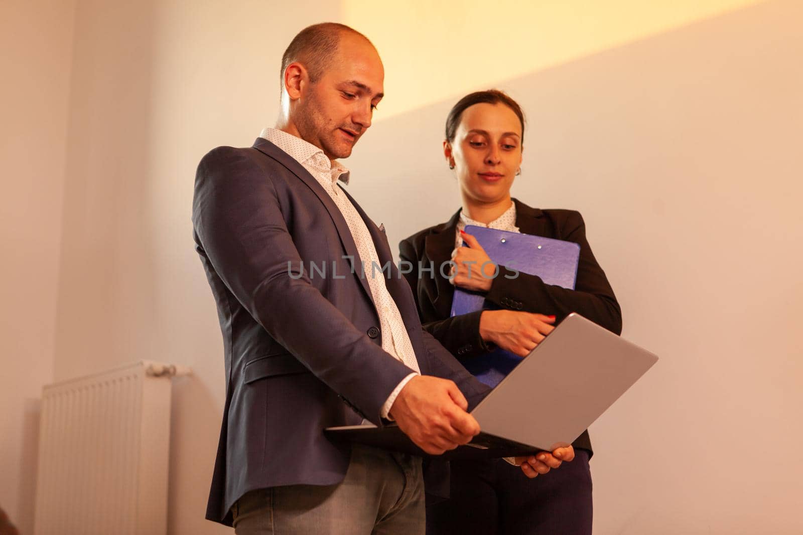 Corporate executive manager holding laptop talking with businesswoman by DCStudio