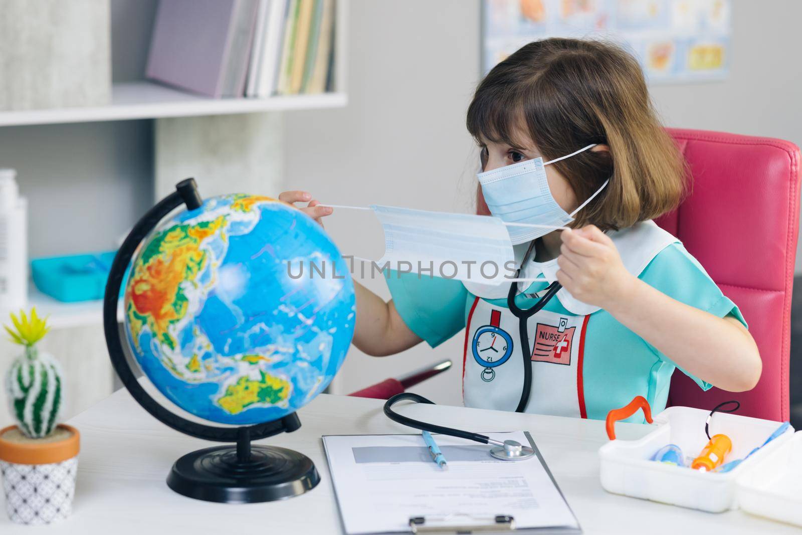 Little cute kid girl doctor puts a mask on the globe of the planet Earth. Save earth planet hands. Our future in your hands. Little girl dressed in a doctor's suit treats the planet Earth
