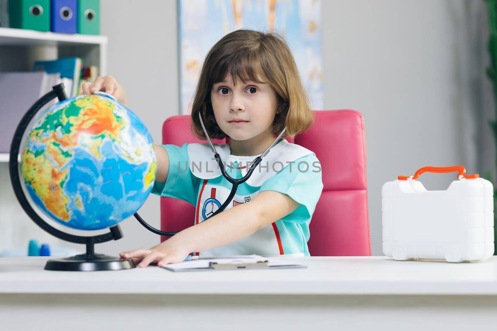Little girl is dressed in medical clothes with a stethoscope in her hands examines and plays a game of healing the planet Earth. World planet earth eco friendly. Sick earth planet Covid-19 symptoms. by uflypro