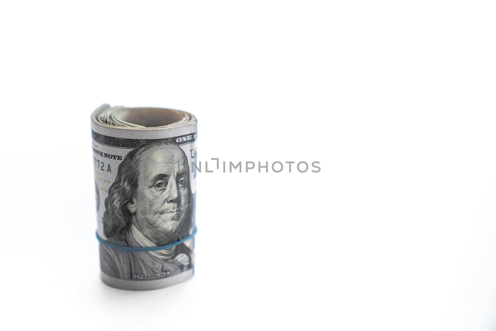 A wad of money is rolled up with a Benjamin or United States hundred dollar bill on the top standing on edge with a blue rubber band isolated on a white background with copy space.