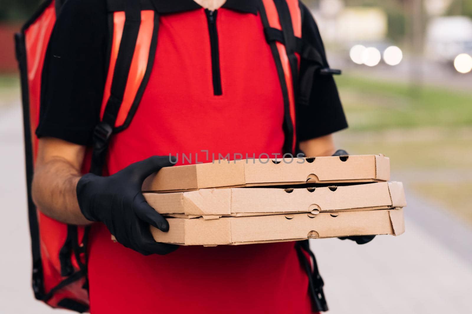Delivery man holding three pizza cardboard boxes at city street, food deliveryman in protective medical face mask, gloves, Coronavirus COVID-19 epidemic quarantine outbreak. Delivery services. by uflypro
