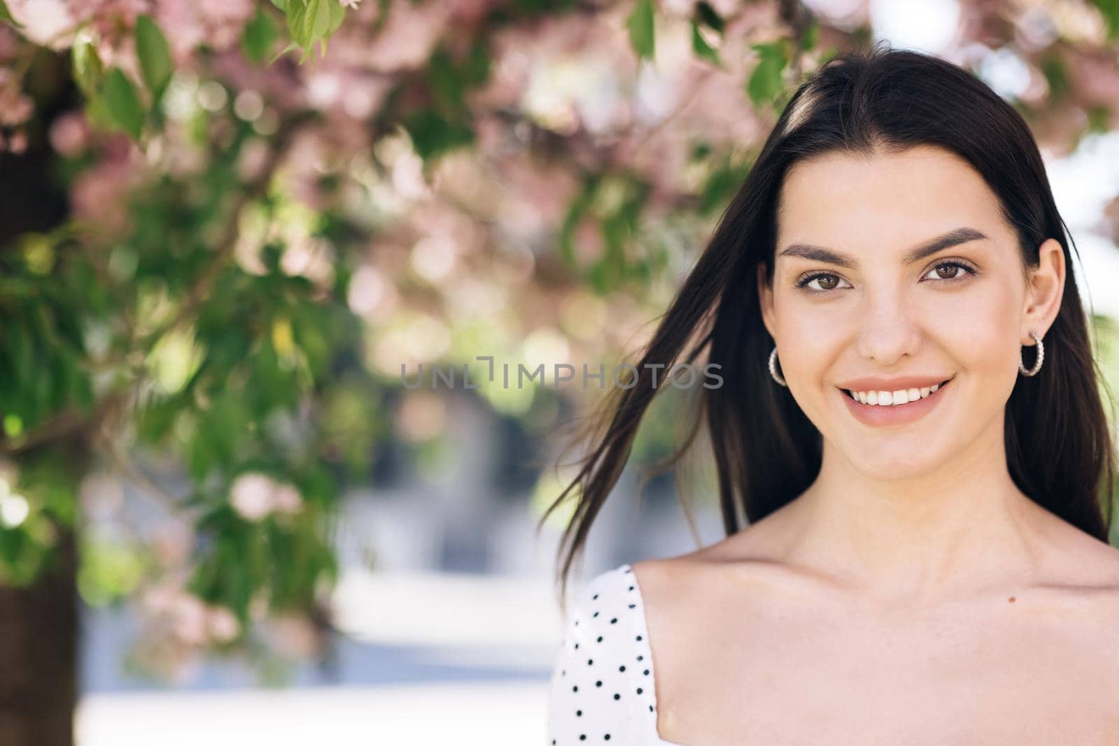 Beautiful smiling confident young ethnic woman pretty face looking at camera posing alone at park on a background of sakura trees. Happy millennial ethnicity girl student professional front portrait. by uflypro
