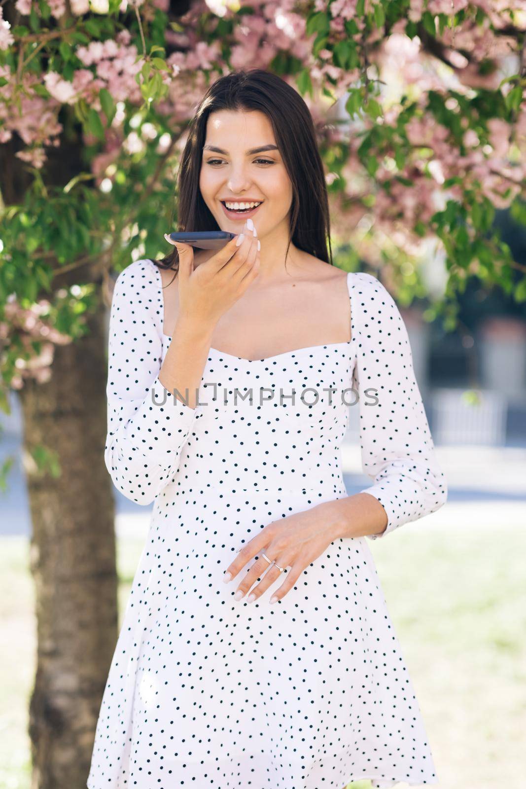 Happy young girl using smart phone voice recognition, dictates thoughts, voice dialing message outdoor talking to mobile assistant. Talking mouth in the speaker of a young woman by uflypro