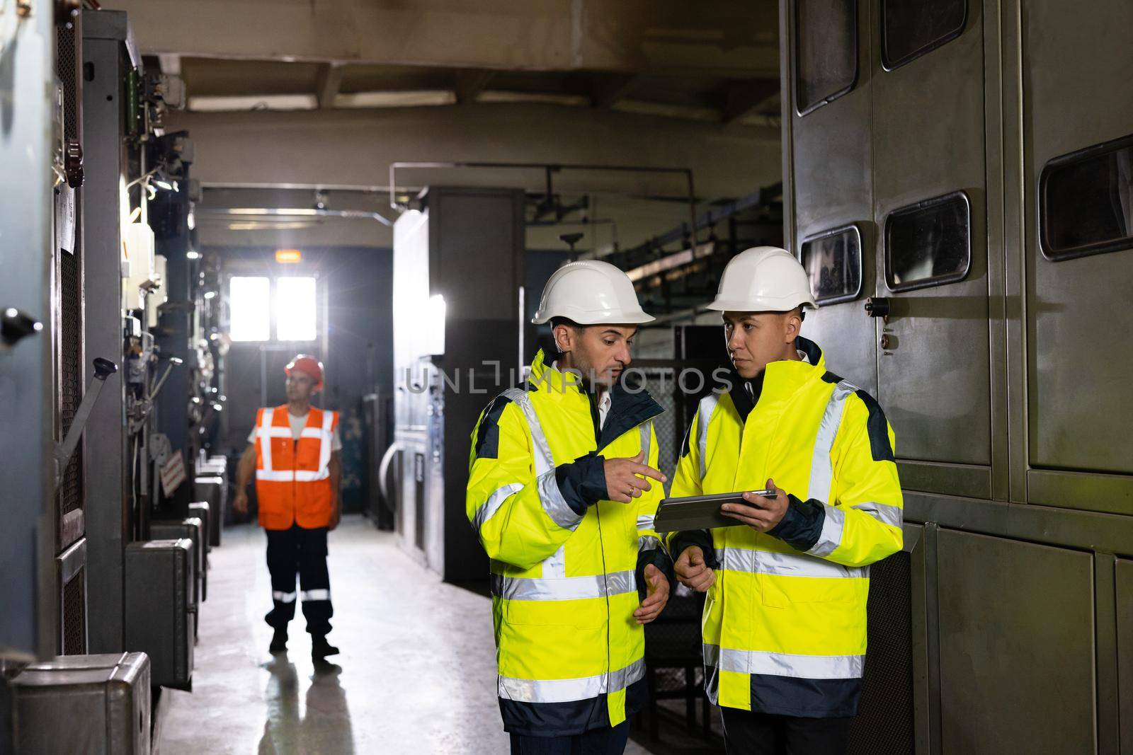 Male Electrical Engineers in Hard Hats Discuss New Project while Using Tablet Computer. They're Making Calculated Engineering Decisions. They Work at the Electric Power Factory.