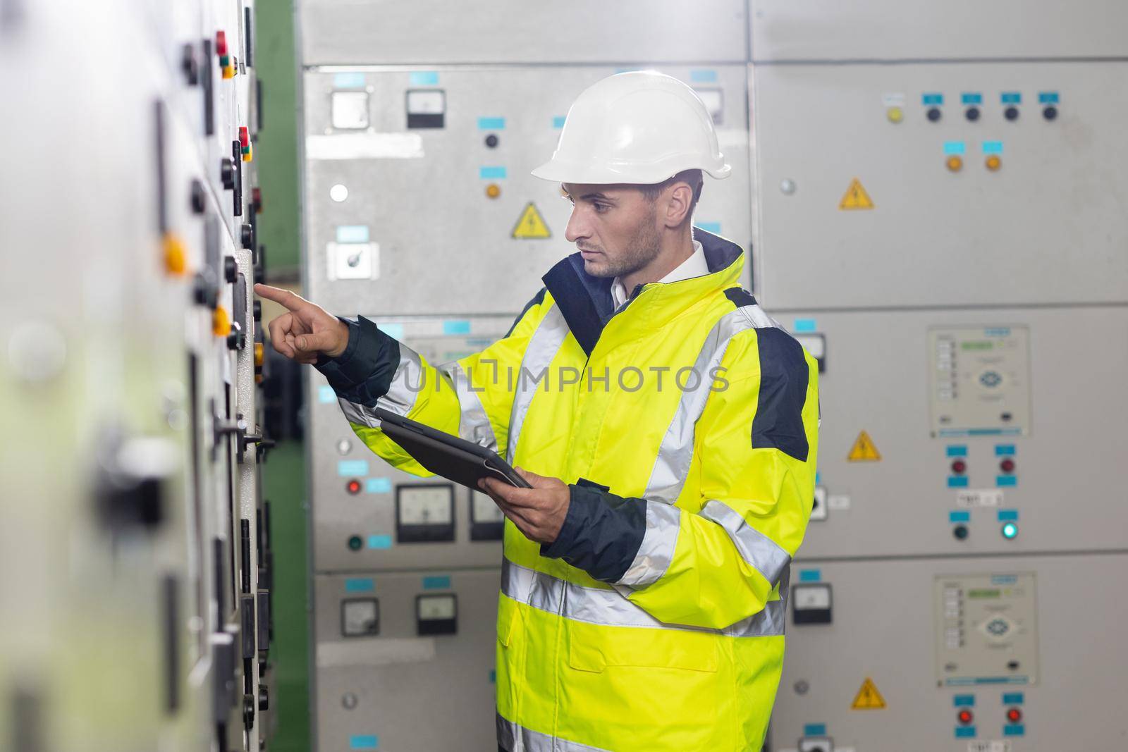 Man electrical engineer hold tablet monitoring electrical system in control room. Technician inspect to control panel screen system for generate electricity of factory in manufacture industrial.