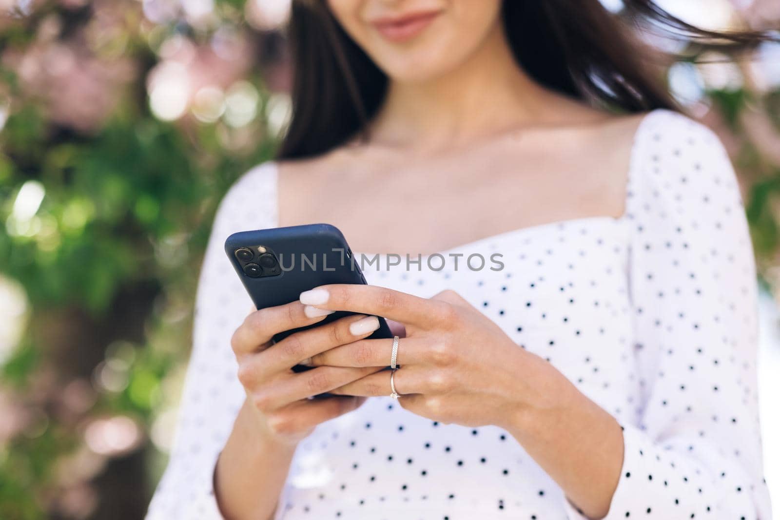 Woman wearing white dress using smartphone. Girl using social media application text messages receive news smiling outdoor. Communication, social networks, online shopping concept. Technology.