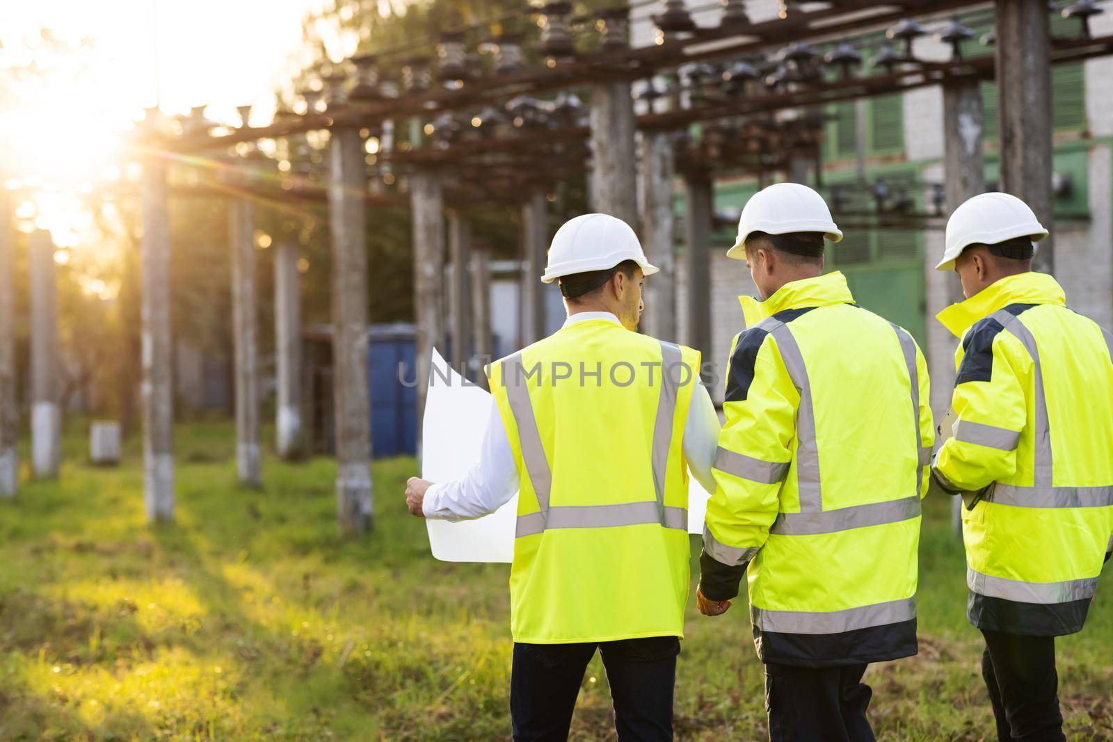 Back view group of diverse specialists in the middle of construction site they analyzing the plan of the construction together. Electric industry, electrical energy production concept by uflypro