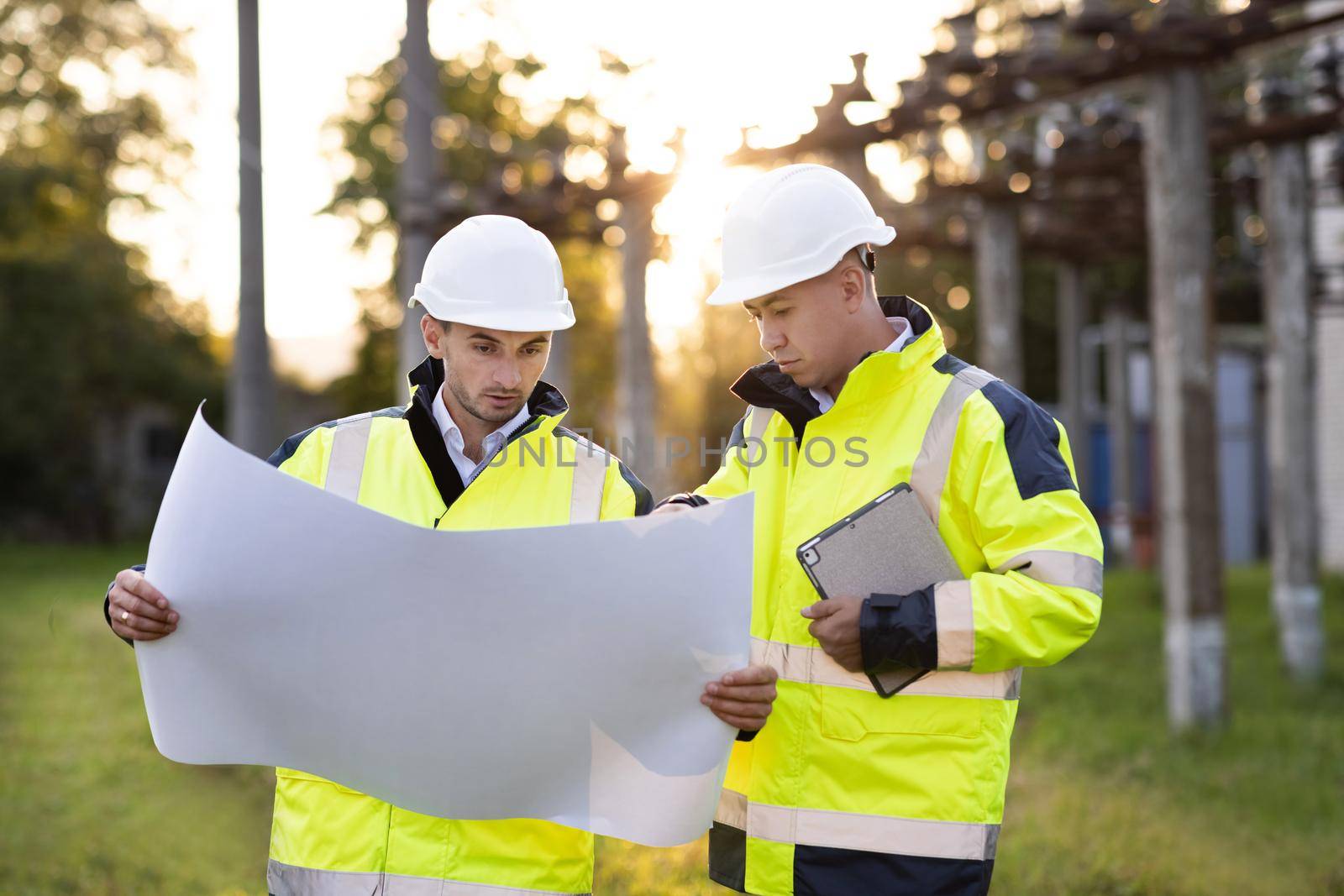 Group of Industry Engineer discussion with Blueprints checking information and safety system at Industrial Manufacturing Factory. Two worker talking with paper work at sunset. by uflypro