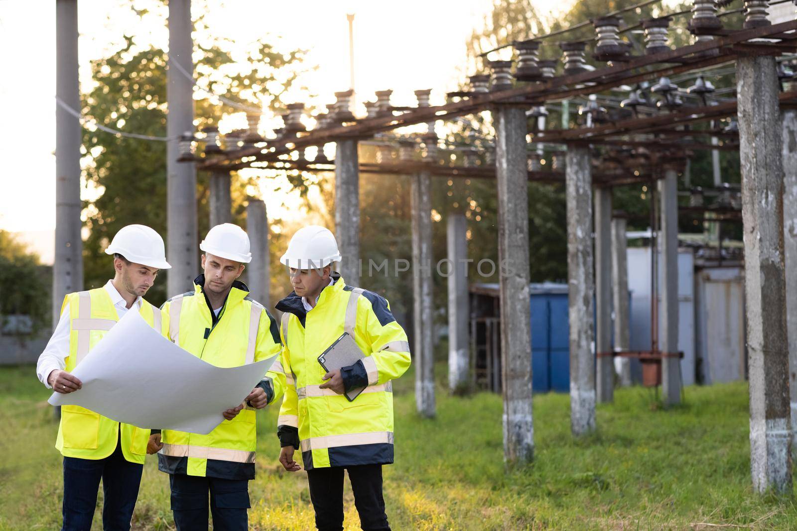 Power specialists are planning a new project outdoors. Three engineers walk near power lines in the high voltage power station. Electric industry, electrical energy production concept by uflypro