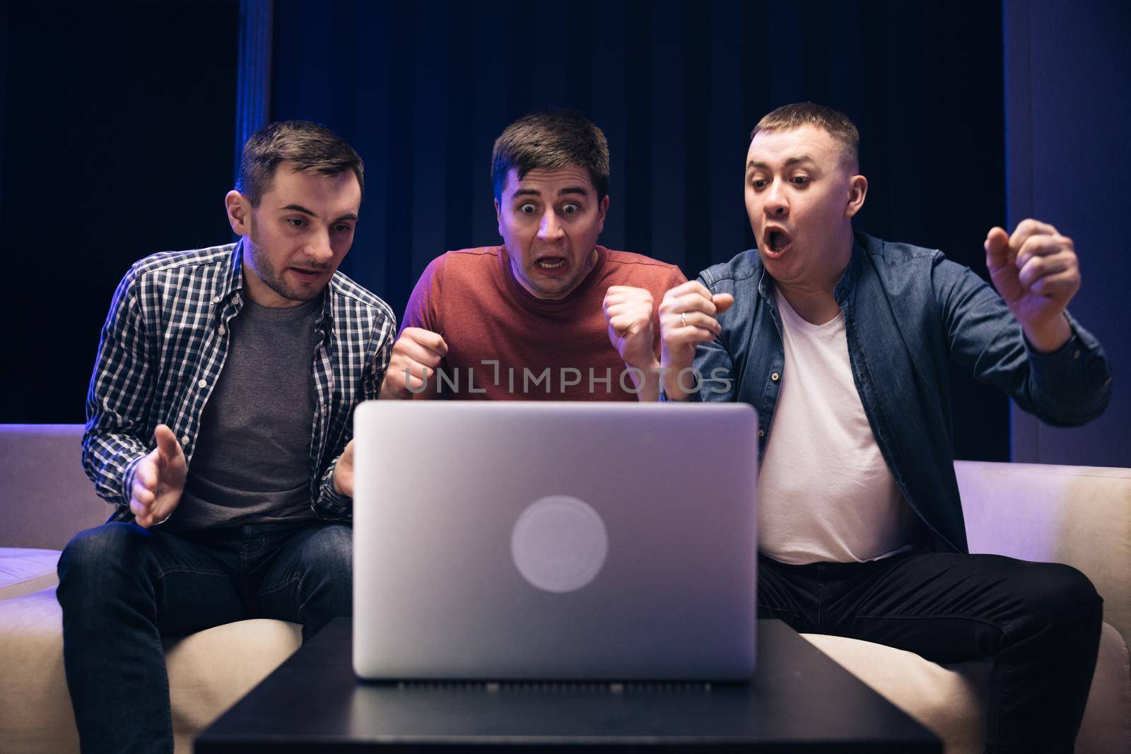 Male friends watching online football game match at laptop. Men fans buddies supporters cheering celebrating victory goal score support winning team. Men watching football in streaming on laptop.