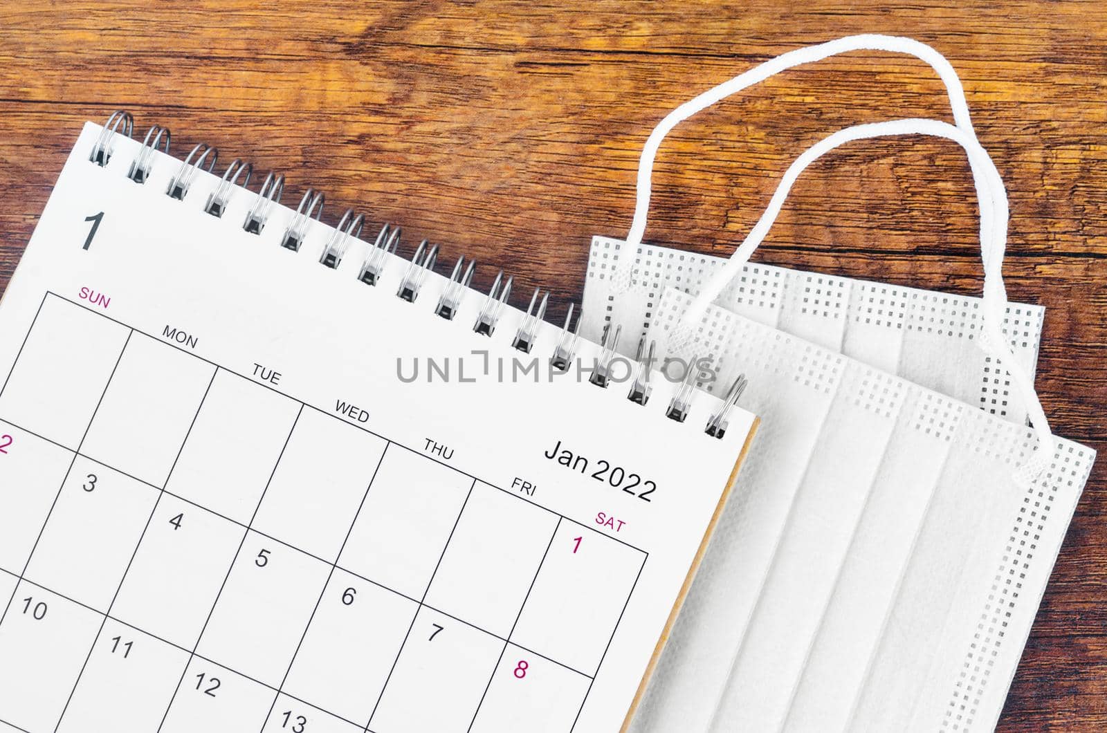 January 2022 desk calendar with surgical mask medical on wooden background.