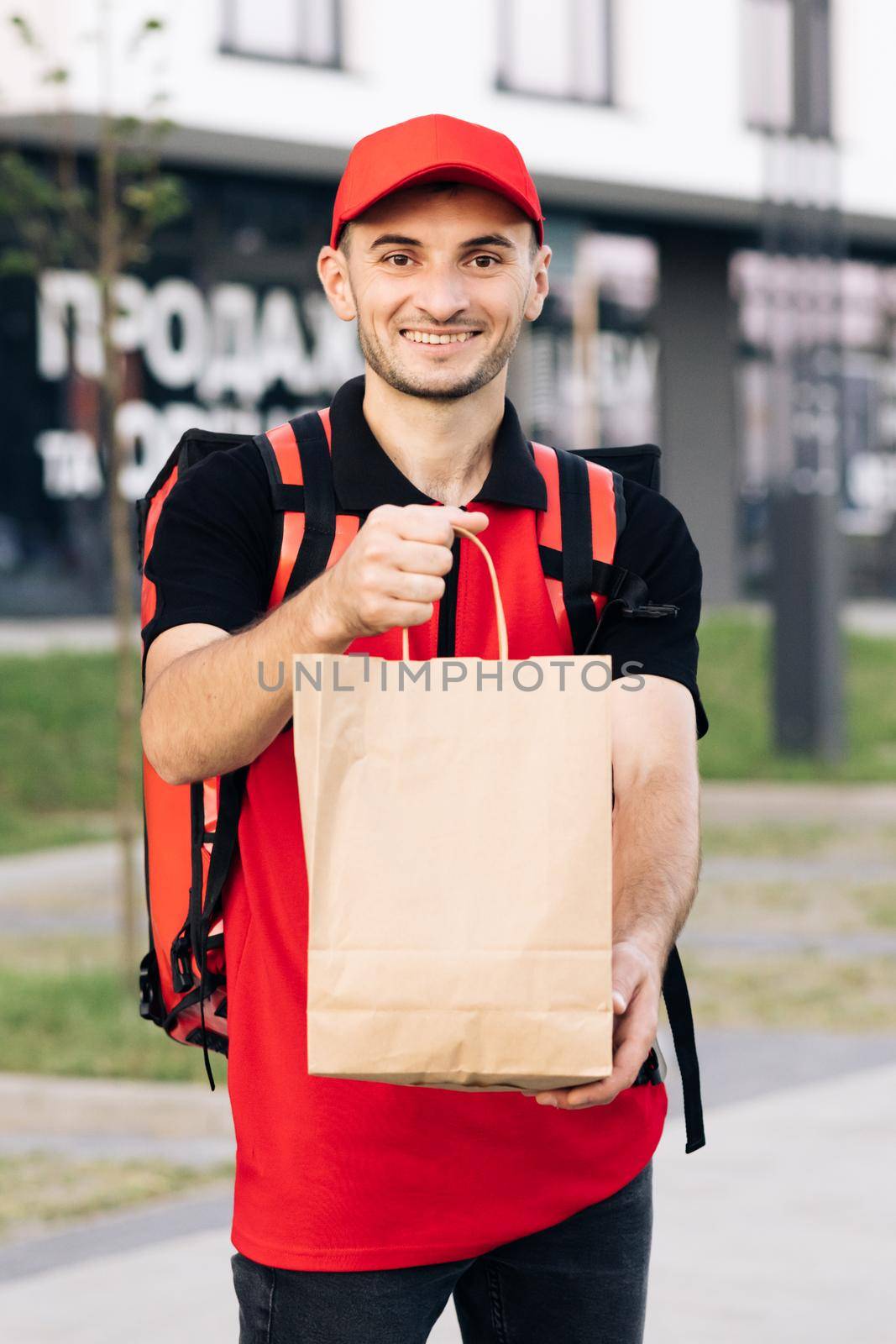 Food delivery man order from a restaurant. Handsome young man in a T-shirt and a cap. Happy delivery worker holding packet with food smiling. Delivery service door to door by uflypro