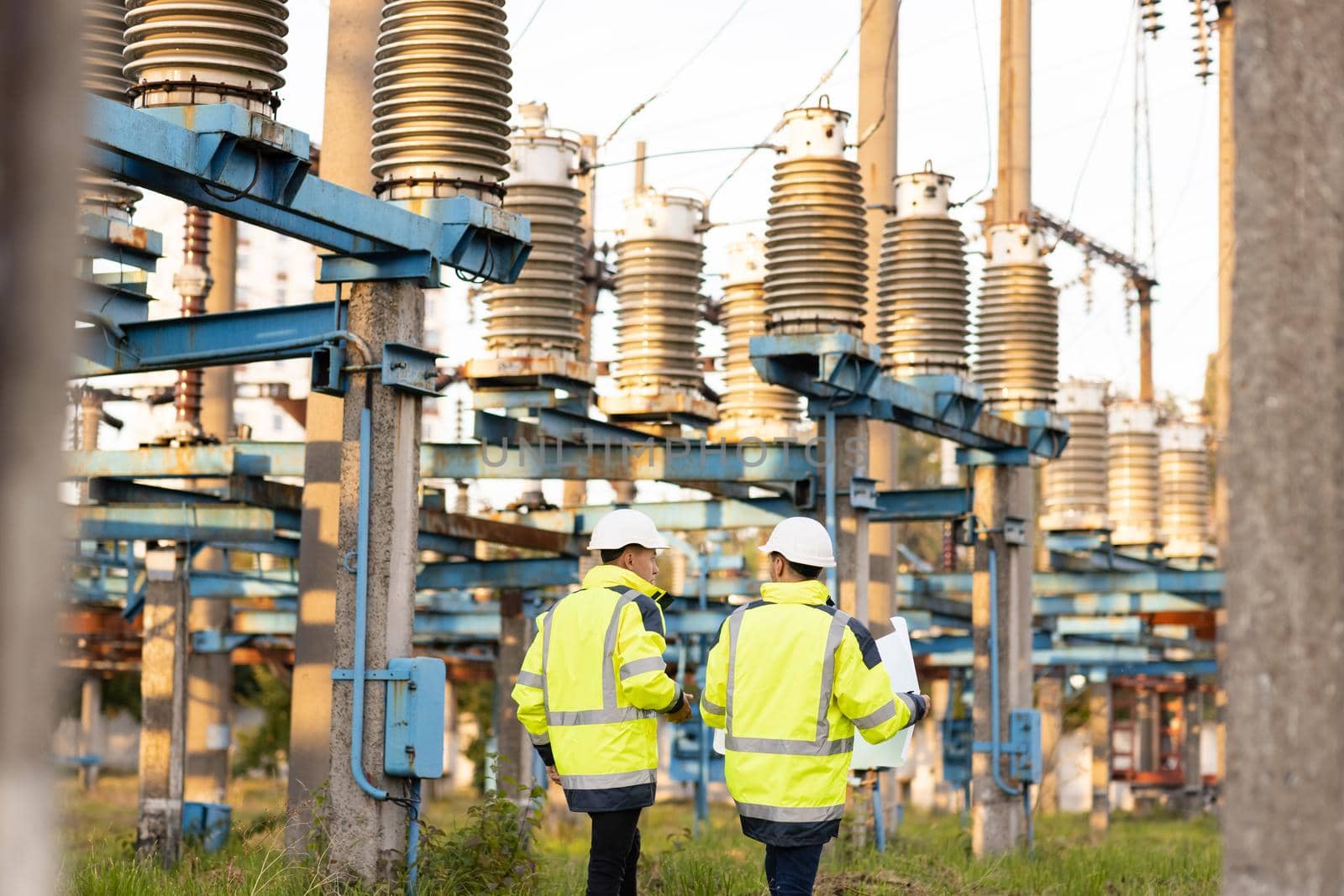 Engineers men in warm clothes use digital tablet computer discuss work walking against power electric substation.