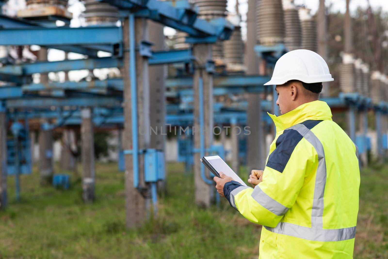 Electrical worker engineer working with digital tablet near tower with electricity. Energy business technology industry concept. Electrical engineer studying reading on tablet.