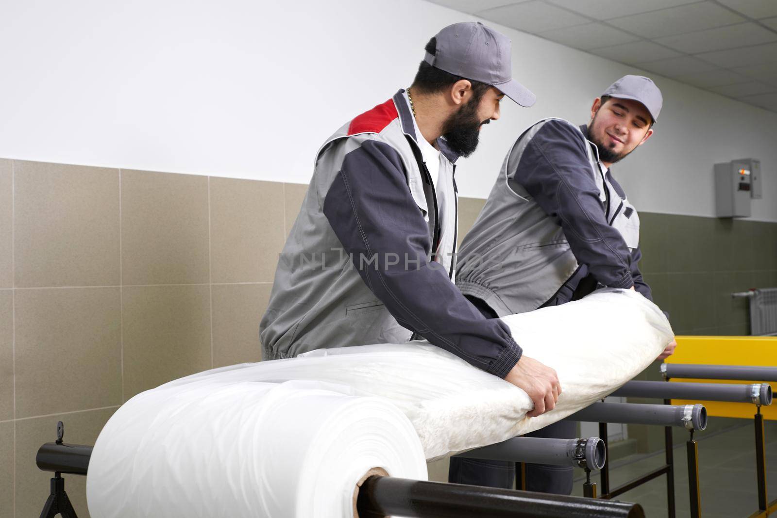 Men workers packing carpet in a plastic bag after cleaning it in automatic washing machine and dryer