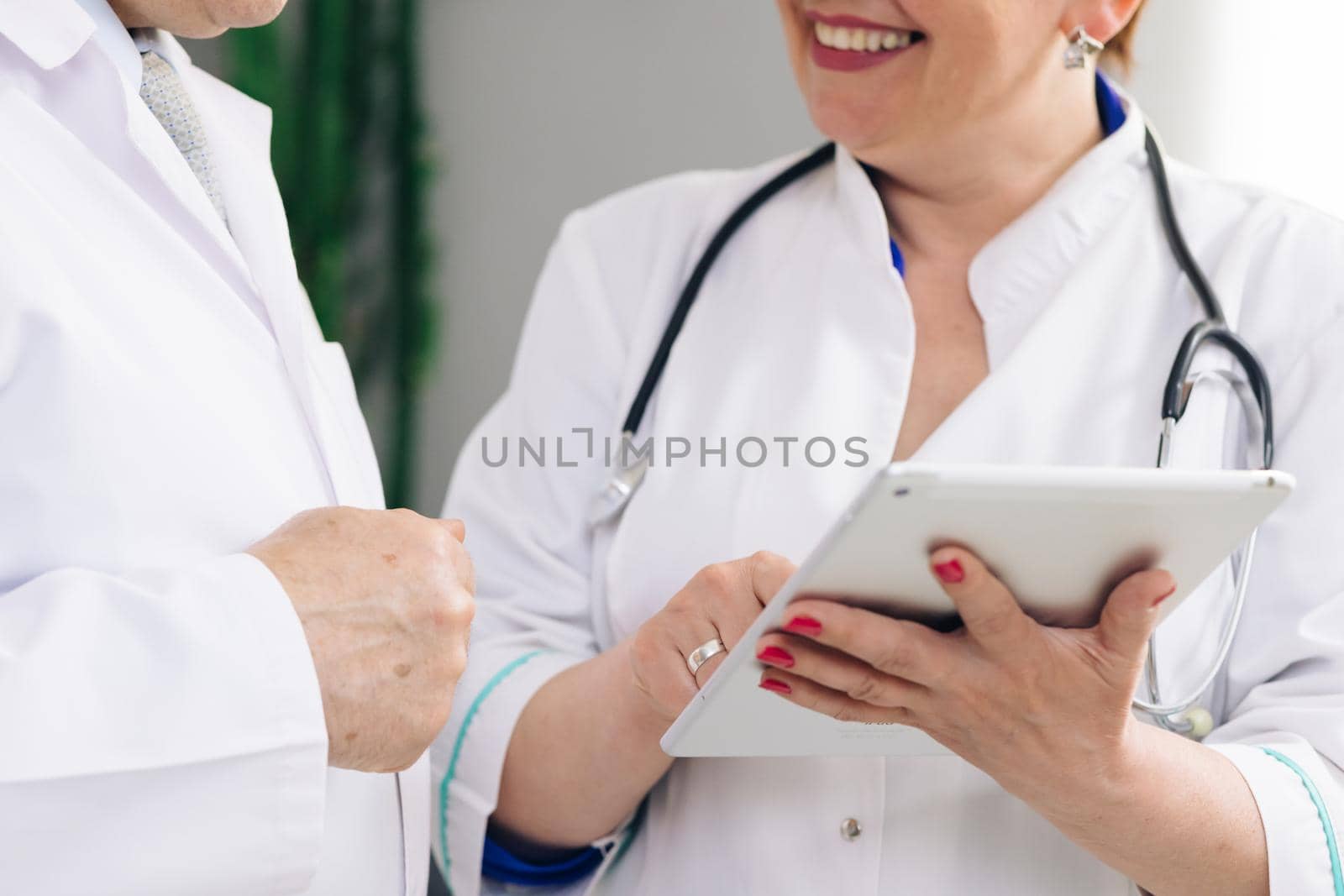 Closeup view of man and woman doctors using tablet during working day at clinic. Caucasian person and his female colleagues use electronic device and work together while standing indoors