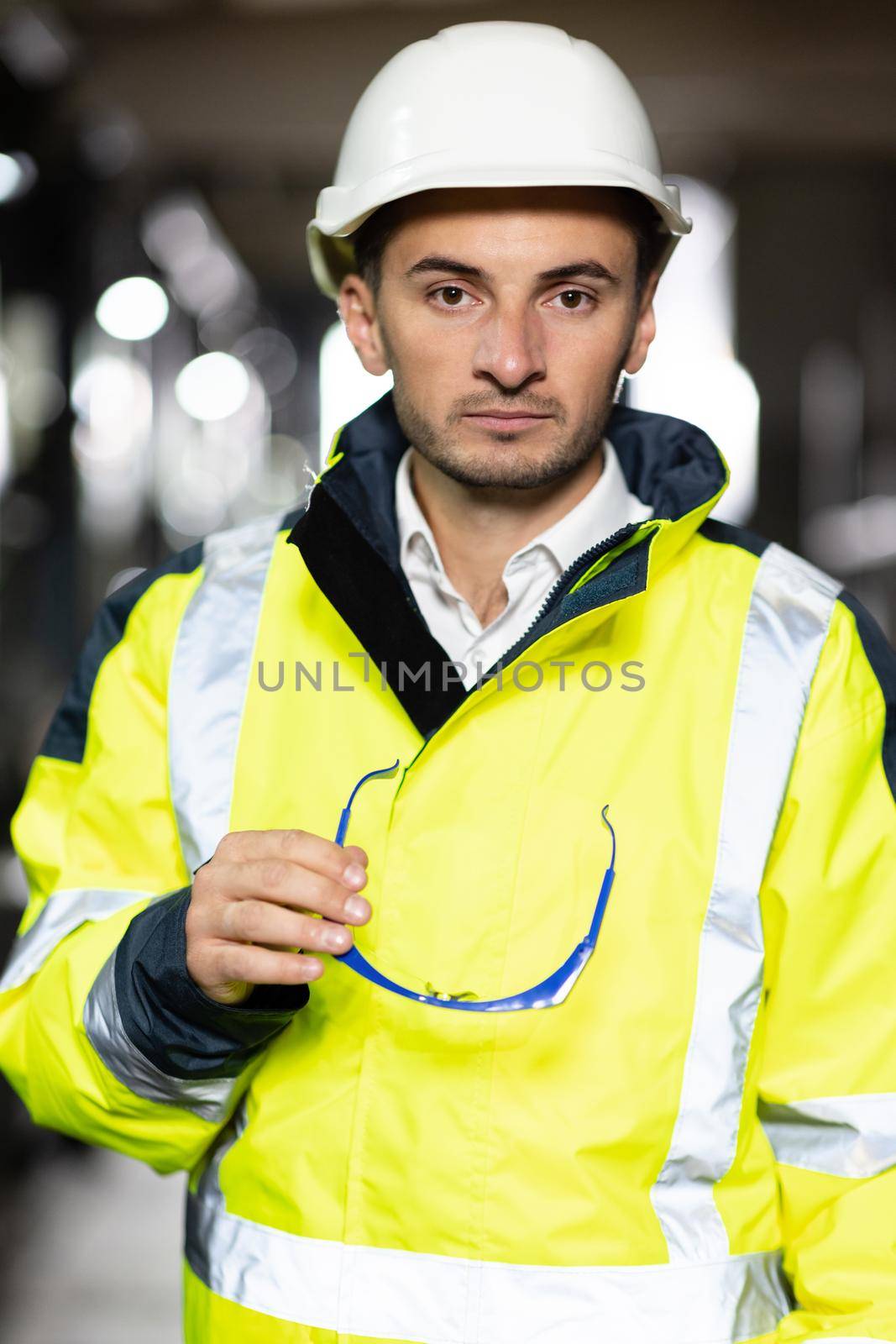 Professional Heavy Industry Engineer Worker Wearing Uniform, Glasses and Hard Hat in a Steel Factory Looks at Camera. Caucasian Industrial Specialist Standing in a Metal Construction Manufacture.