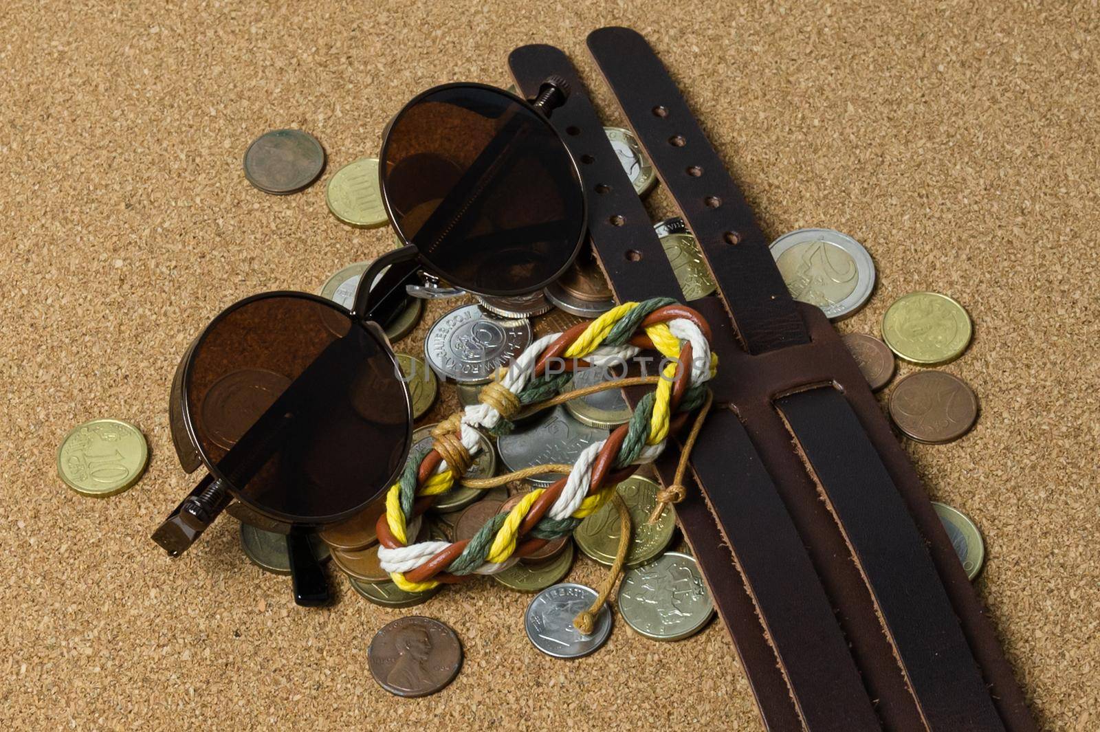 sun glasses with various bracelets and coins rest casually on the light brown leather on a flat surface