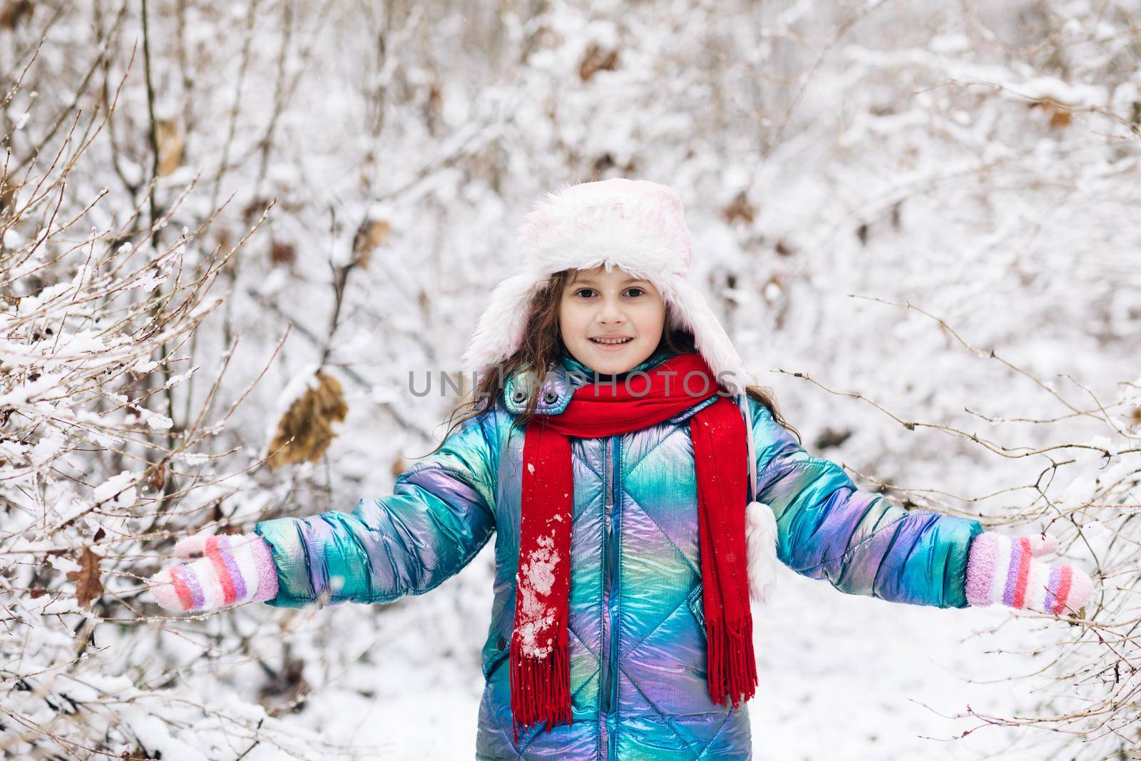 Happy child girl playing with snow on snowy winter walk. Happy winter time. Happy winter moments of joyful young girl with long brunette hair, winter clothes having fun in snowing time by uflypro