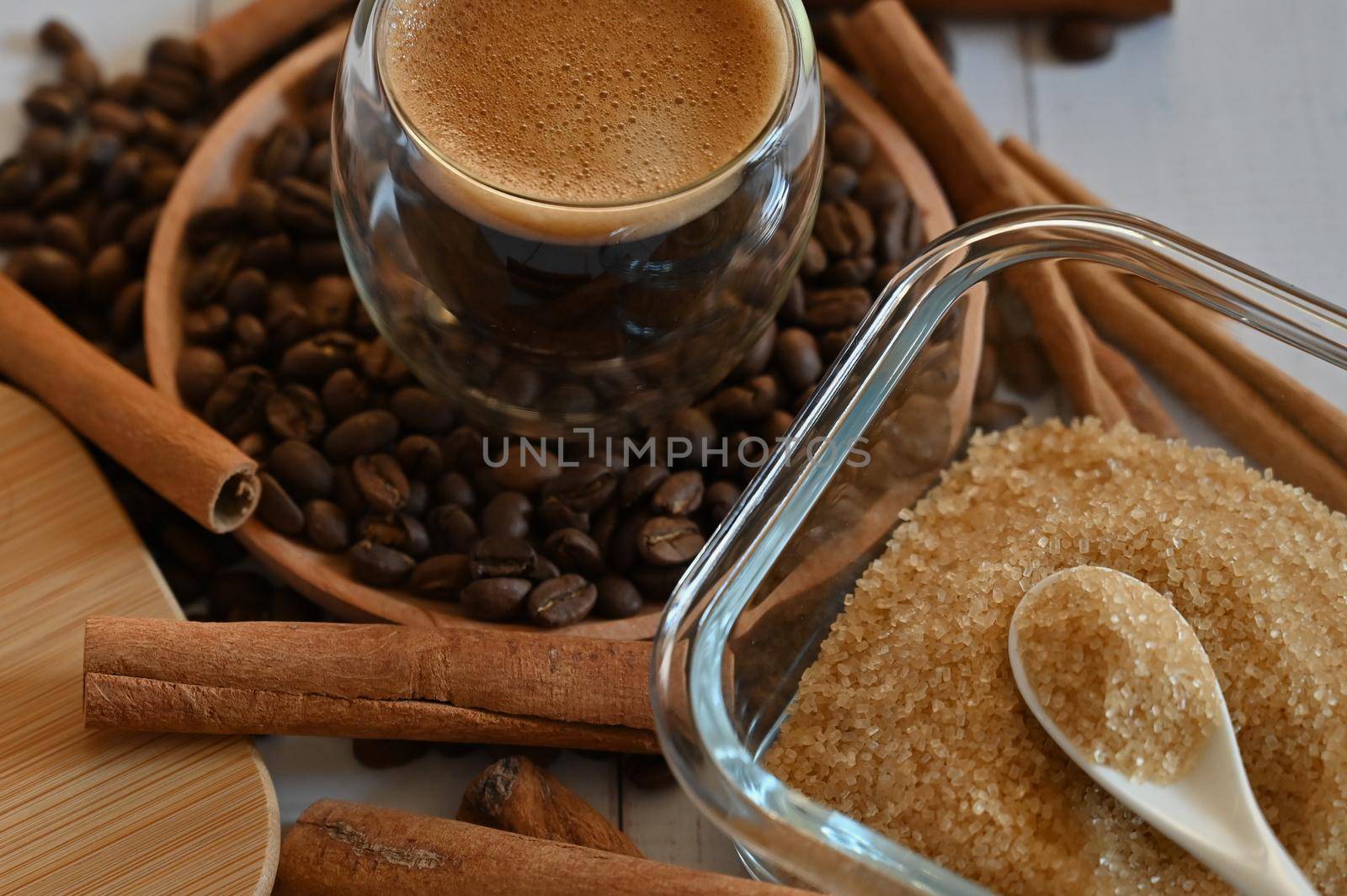 a glass glass stands on coffee beans in a wooden plate next to a sugar bowl with brown sugar close up