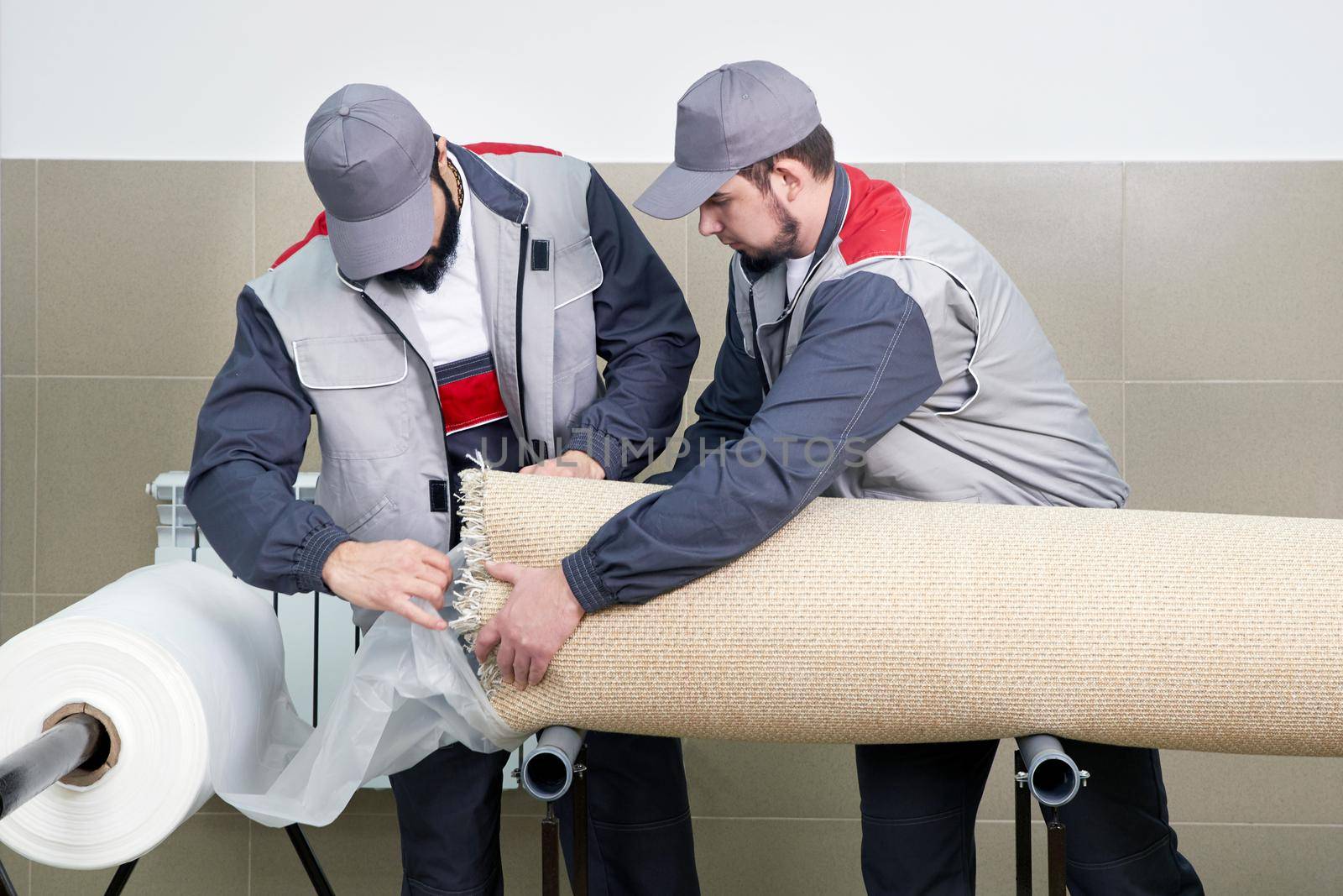 Men workers packing carpet in a plastic bag after cleaning it in automatic washing machine and dryer