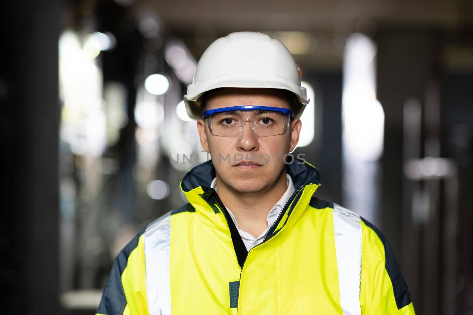 Portrait of employee serious asian man engineer worker wearing safety uniform, goggles and hardhat looking at camera on site factory warehouse background by uflypro