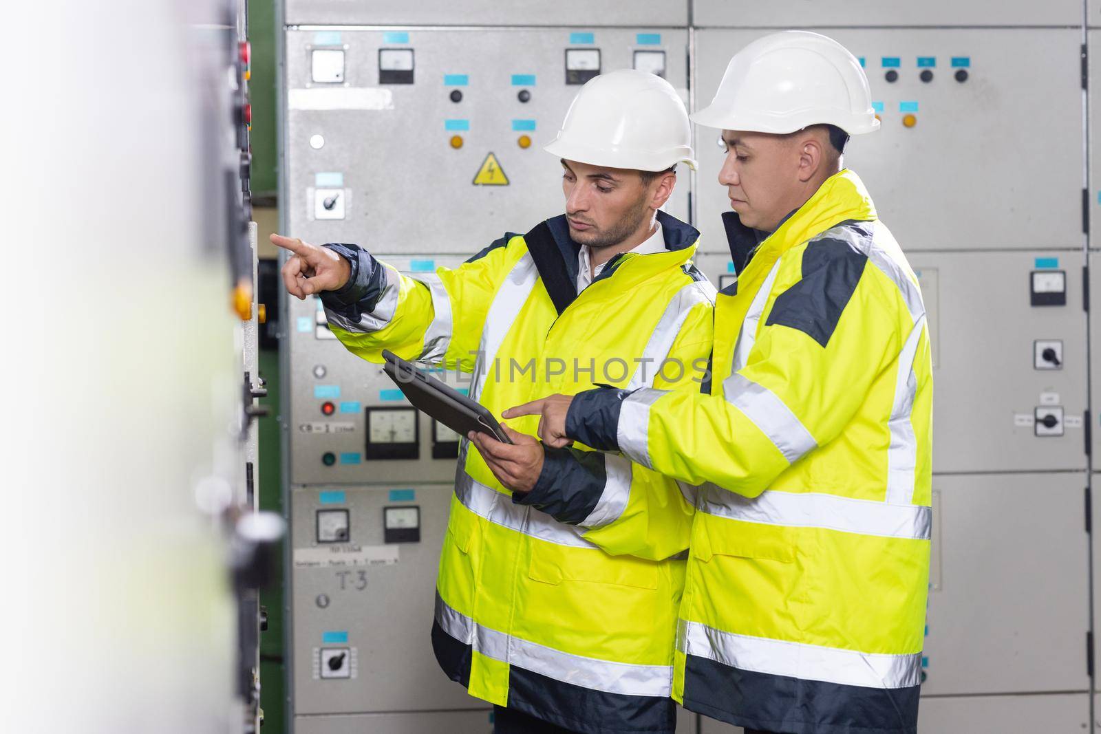 Electrical engineers checking control panel board with tablet. High voltage power station. Electrical engineers standing near therminal box of solar panel.