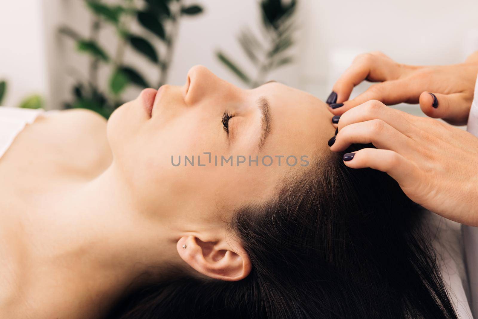 Close up of young girl receiving a facial massage and spa treatment for perfect skin in a luxury wellness center. Caucasian woman lying on spa bed get facial massage from massage therapist at clinic.