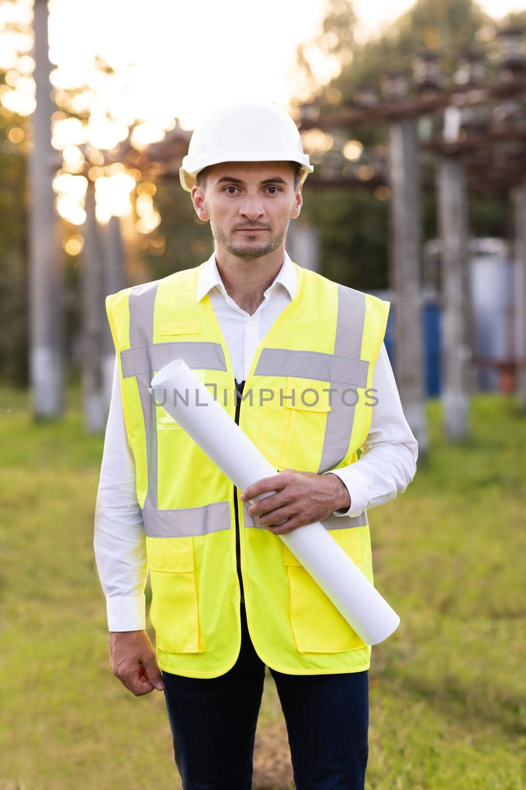 Successful Contractor Investor Architectural Engineer Wearing Hard Hat and Safety Vest Standing on a Commercial Building Construction Site, Crosses Arms Confidently Hold Blueprint in his Hand by uflypro