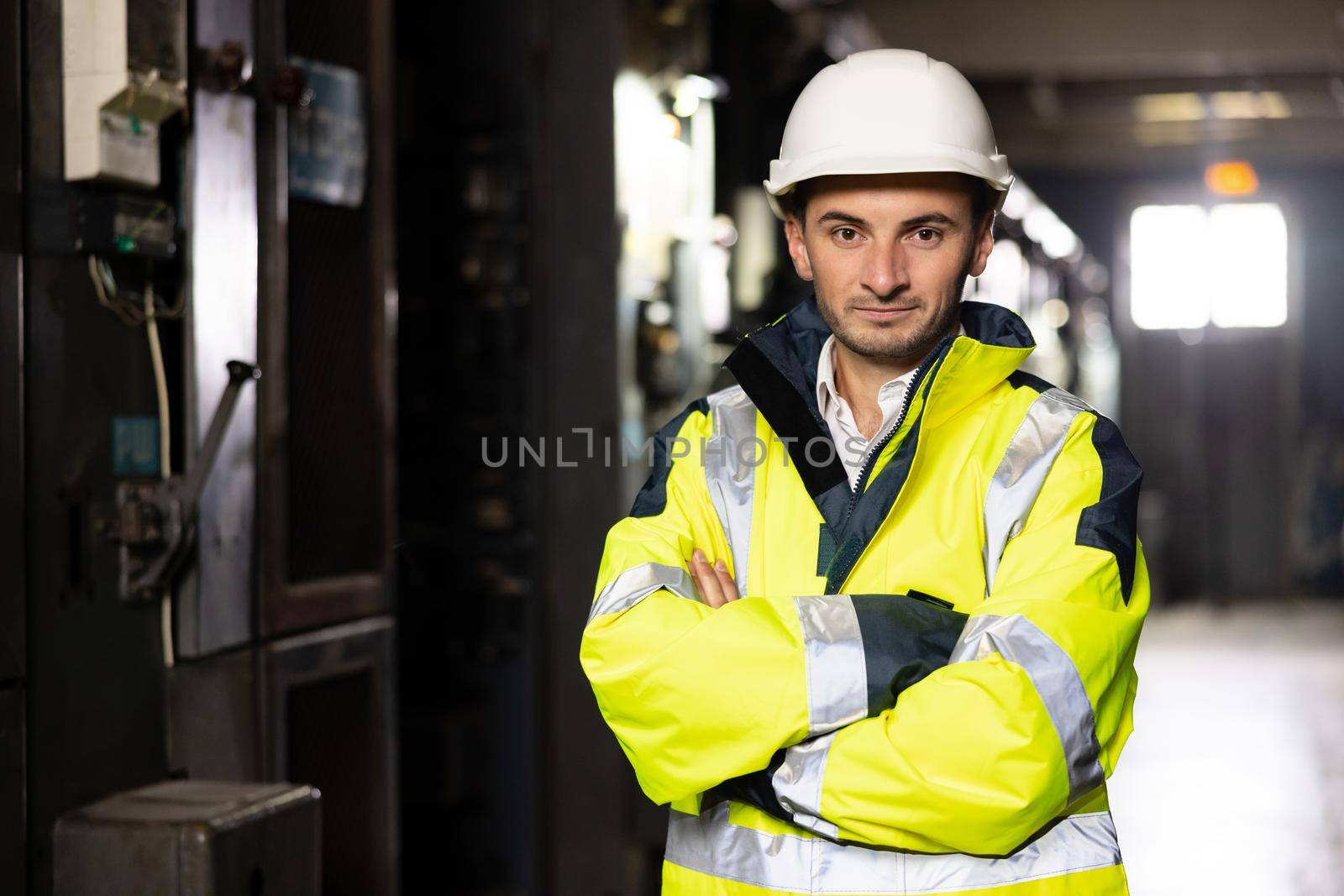 Portrait of young factory engineer or worker wearing safety vest and hard hat crossing arms at electrical control room . Industry and engineering concept.