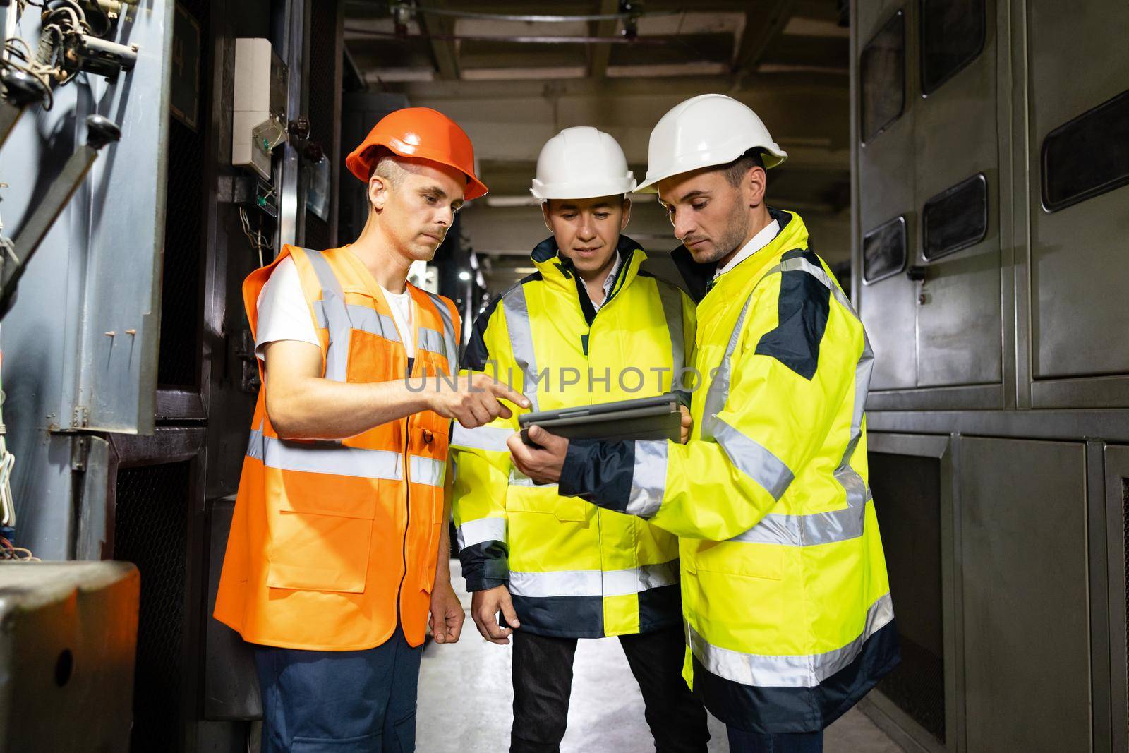 Three engineers men in uniform discuss use tablet, browsing building project indoor of construction site. Businessman worker, man male construction engineers or architects working people by uflypro